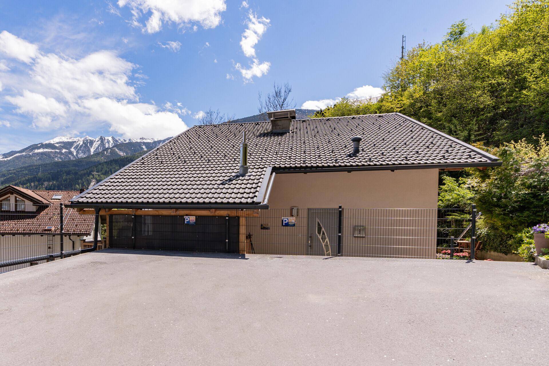 Seitenansicht des Gebäudes mit Satteldach, Carport und Parkplätzen.