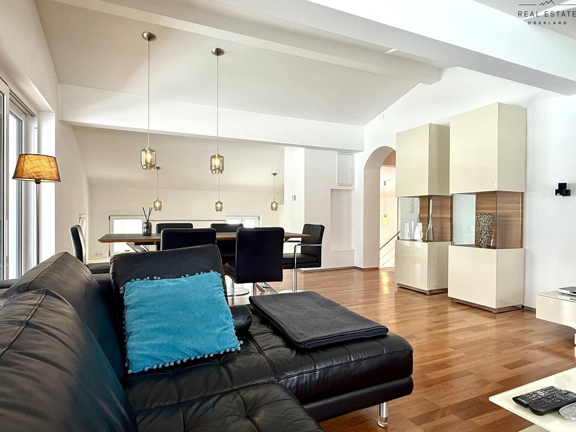 Gemütlicher Wohnbereich mit dunklem Sofa, Blick auf den Essbereich und die offene Küche.