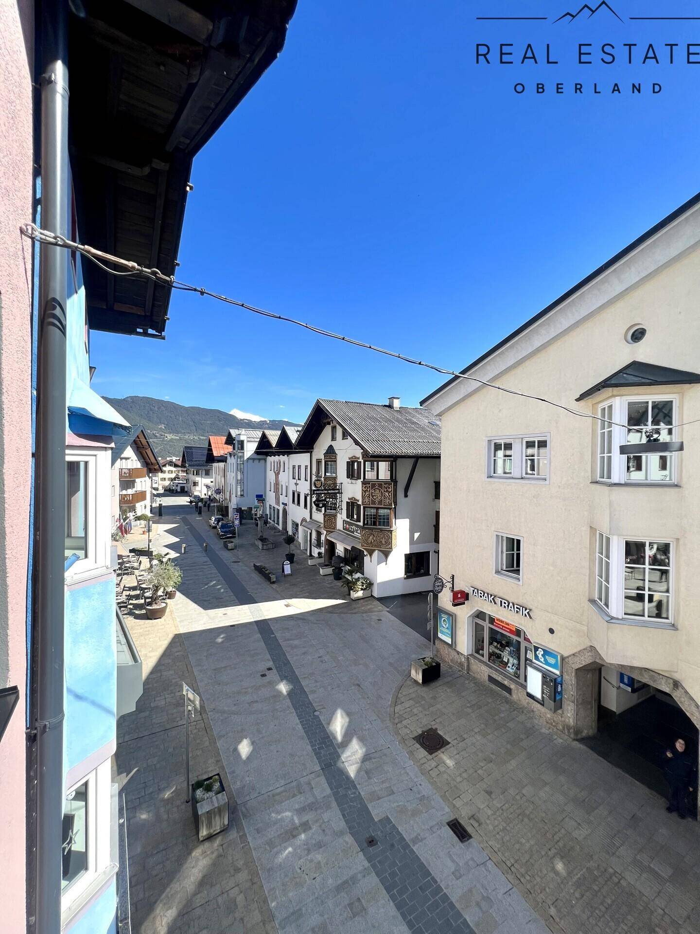 Blick auf die belebte Straße und die umliegenden Gebäude mit Bergpanorama im Hintergrund.