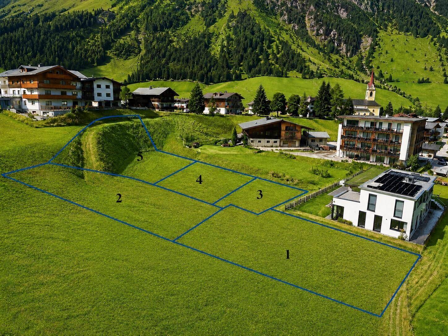 Luftaufnahme von grünen Baugrundstücken mit nummerierten Parzellen und umliegender Berglandschaft mit Kirche.