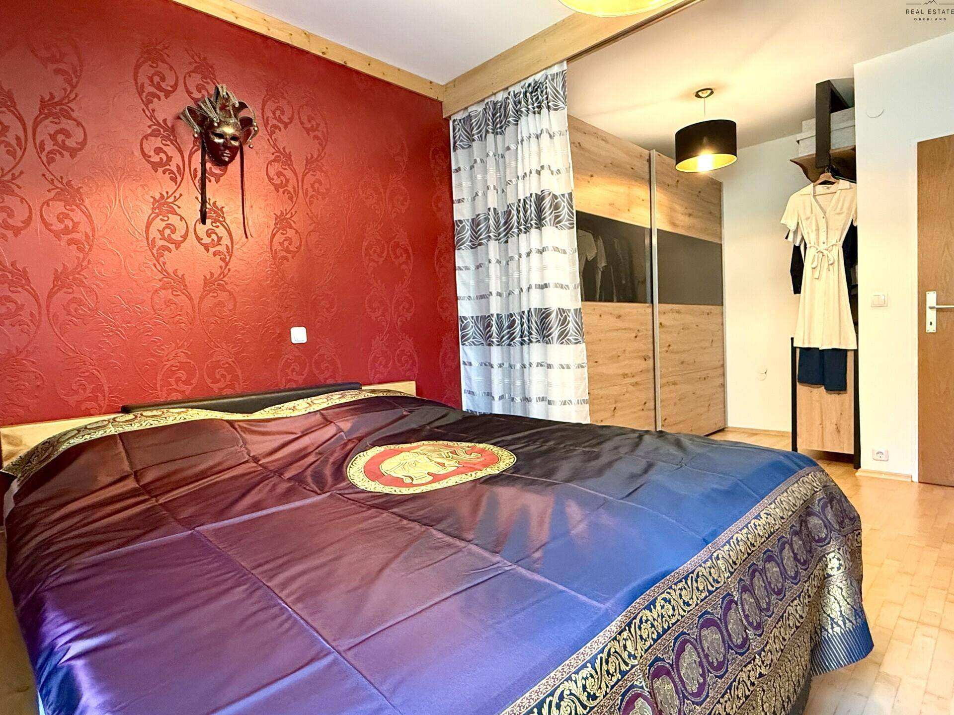 Schlafzimmer mit Holzbett, roter Akzentwand und großem Kleiderschrank.