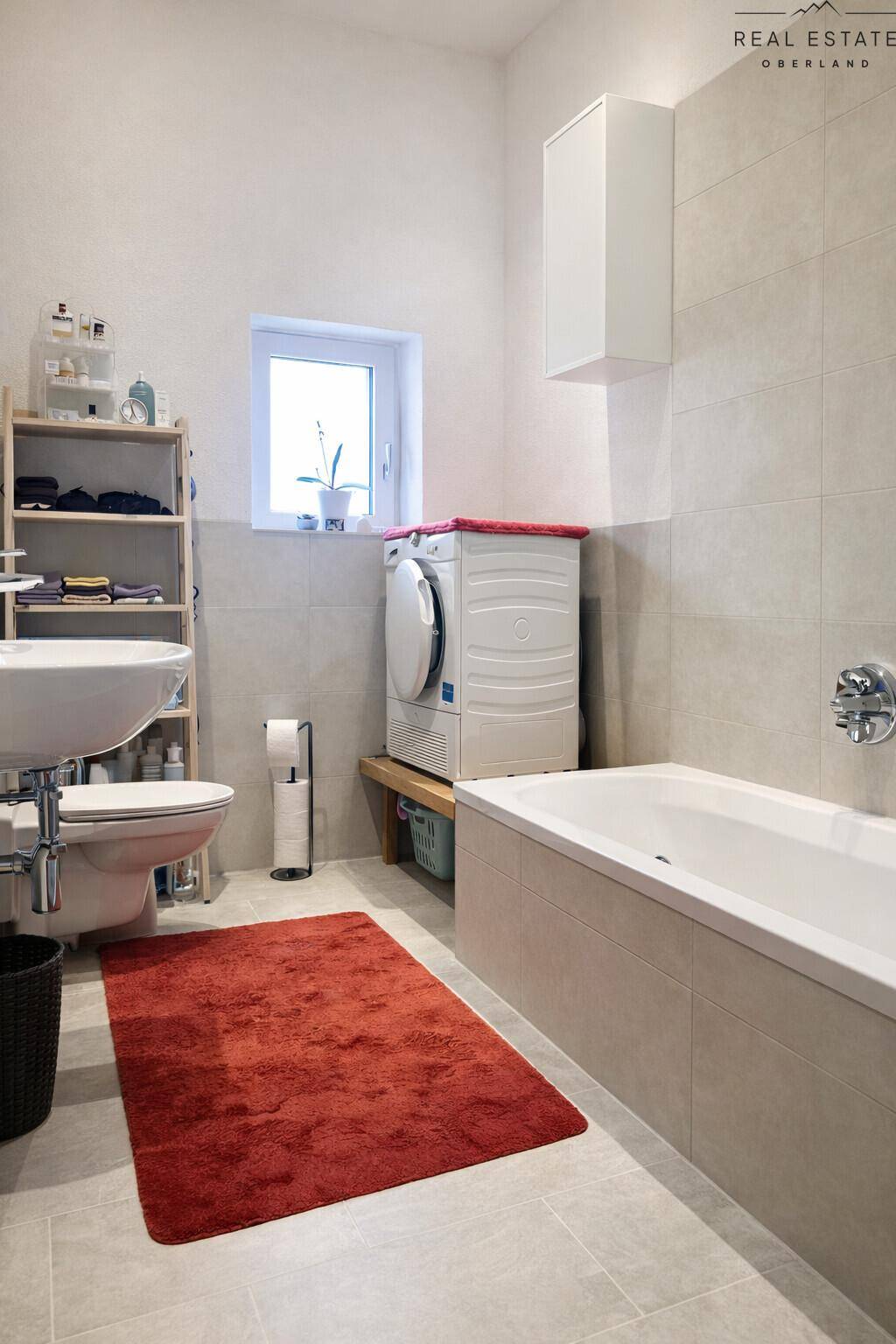 Modernes Badezimmer mit Badewanne, Waschbecken, WC und Waschmaschine, hell gefliest.