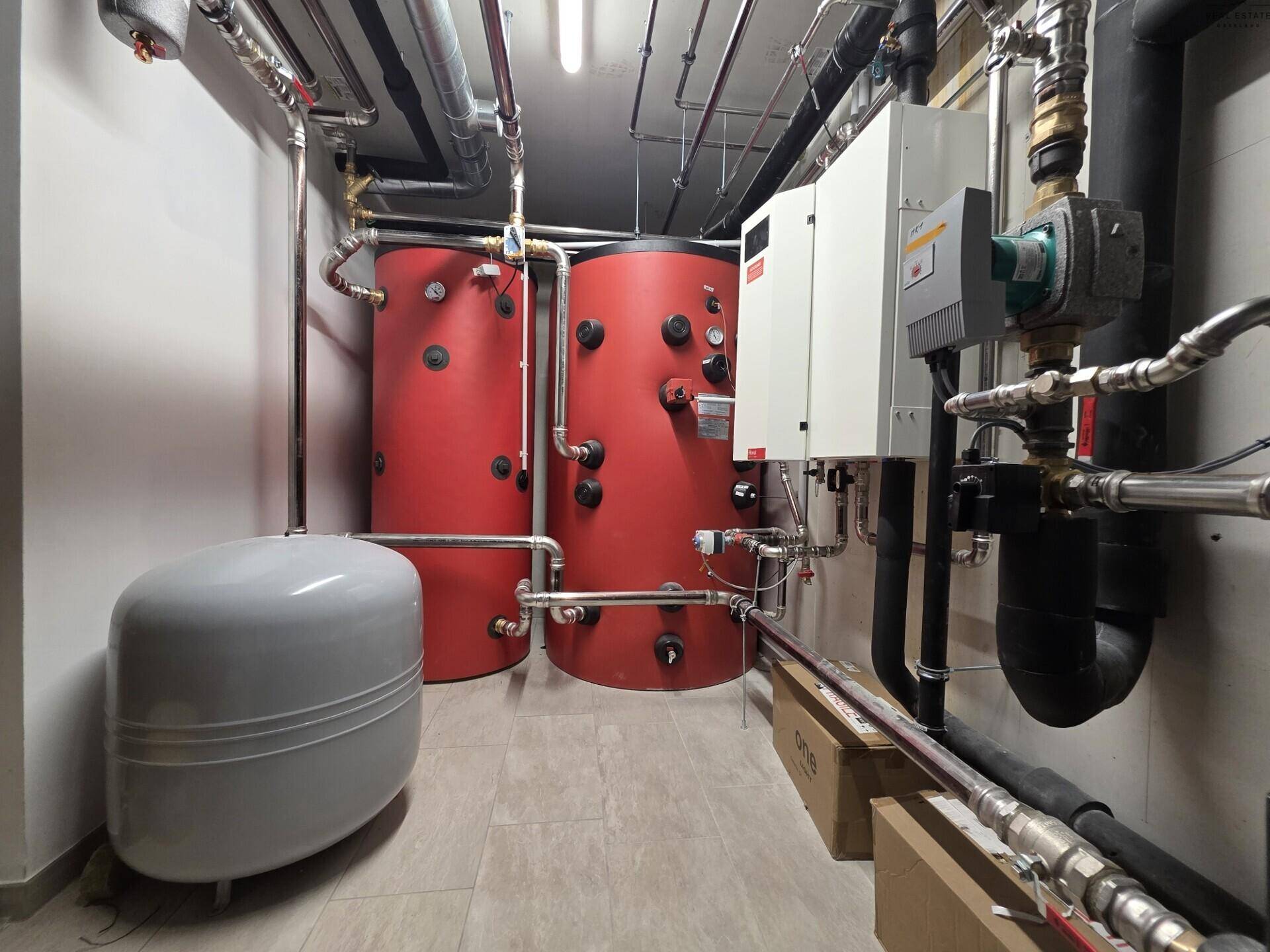 Heizungsraum mit zwei großen Warmwasserspeichern und sichtbaren Rohrleitungen.