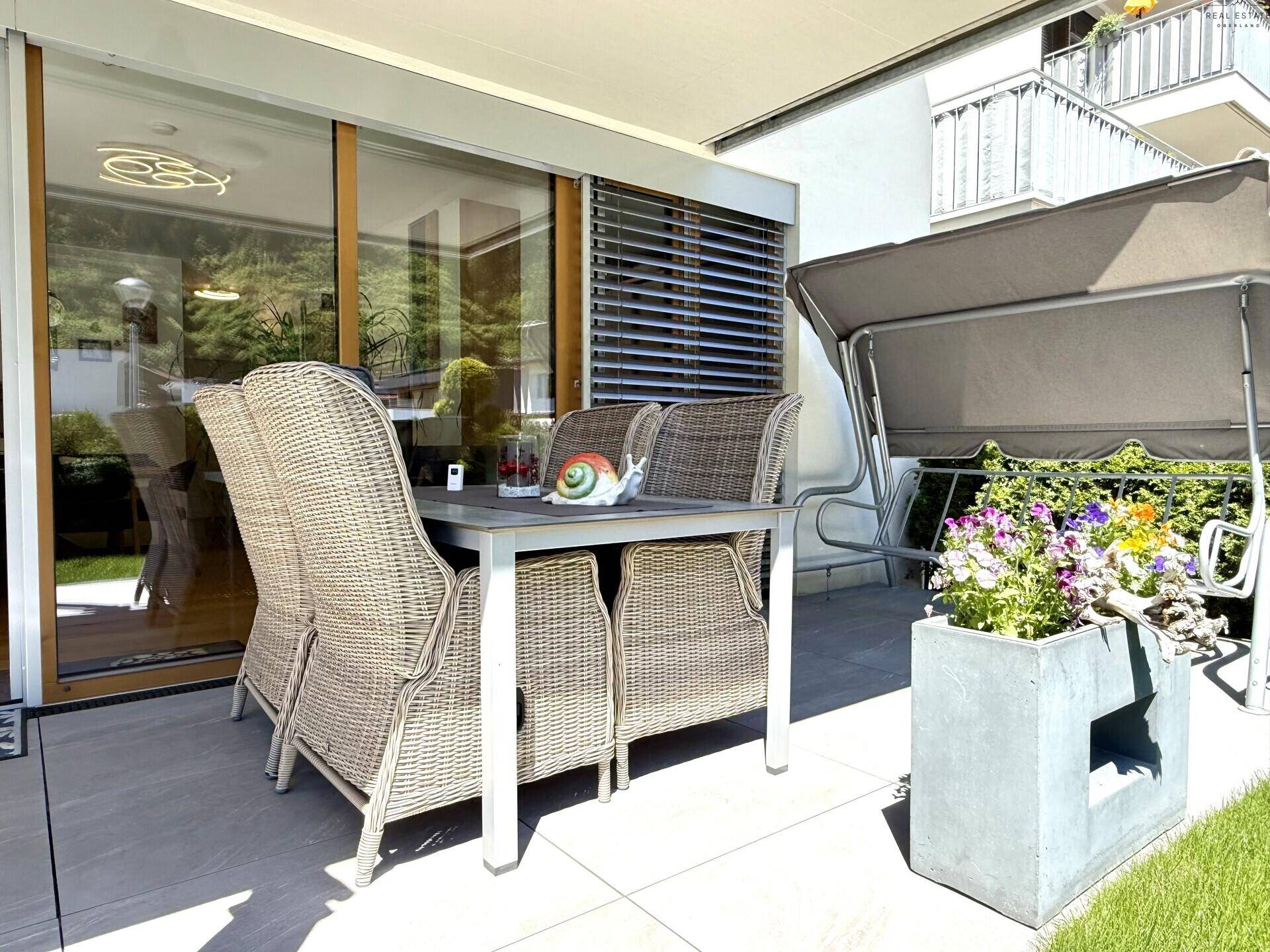 Gemütliche Terrasse mit Rattanmöbeln, Schaukel und Zugang zum Innenbereich.