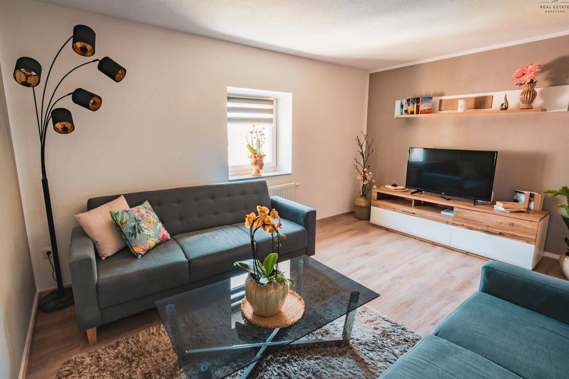 Helles Wohnzimmer mit beigen Wänden, bequemen Sofas und einem Fernseher auf Holzmöbeln.