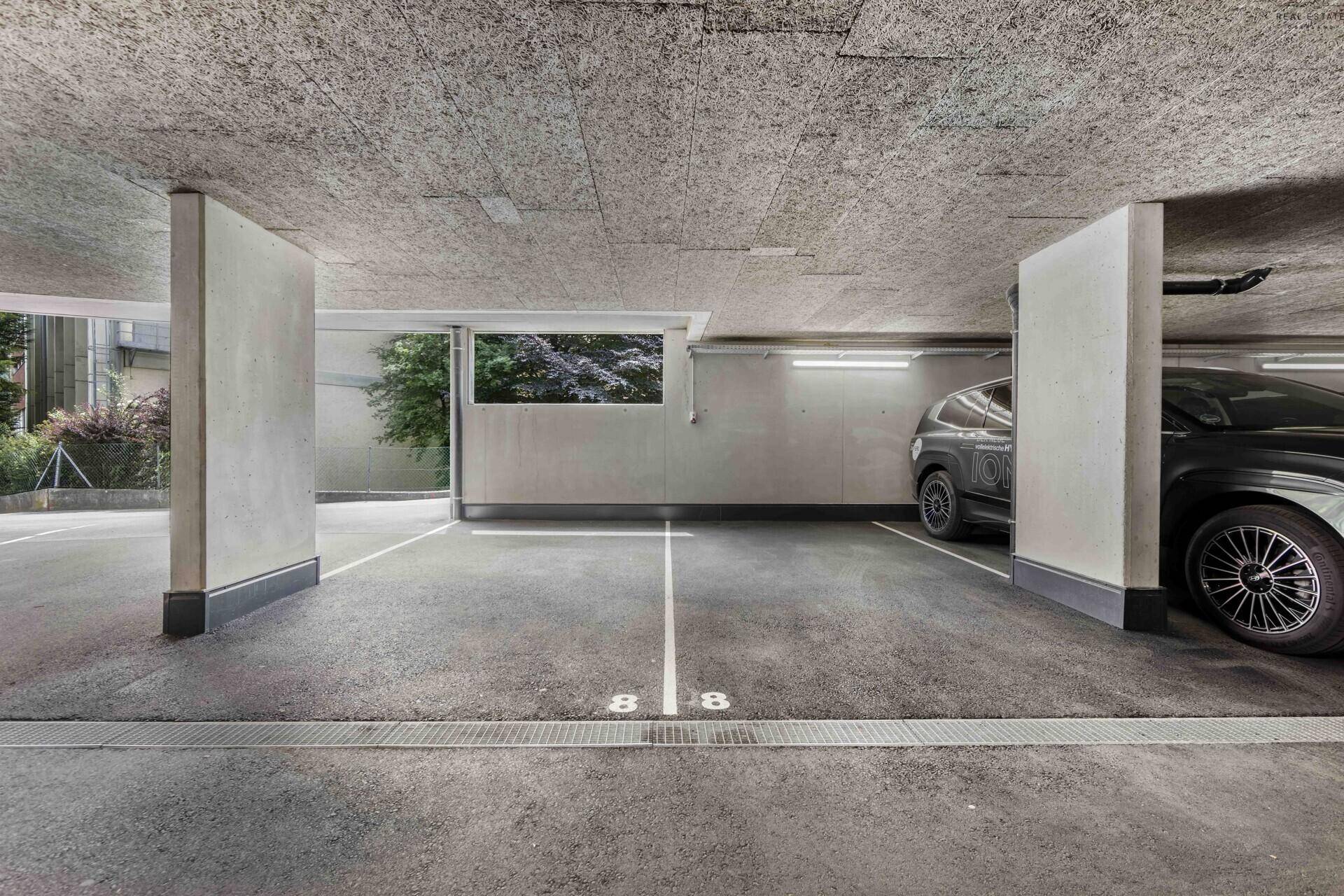 Helle Tiefgarage mit ausreichend Platz für Fahrzeuge, inklusive eines geparkten Autos.