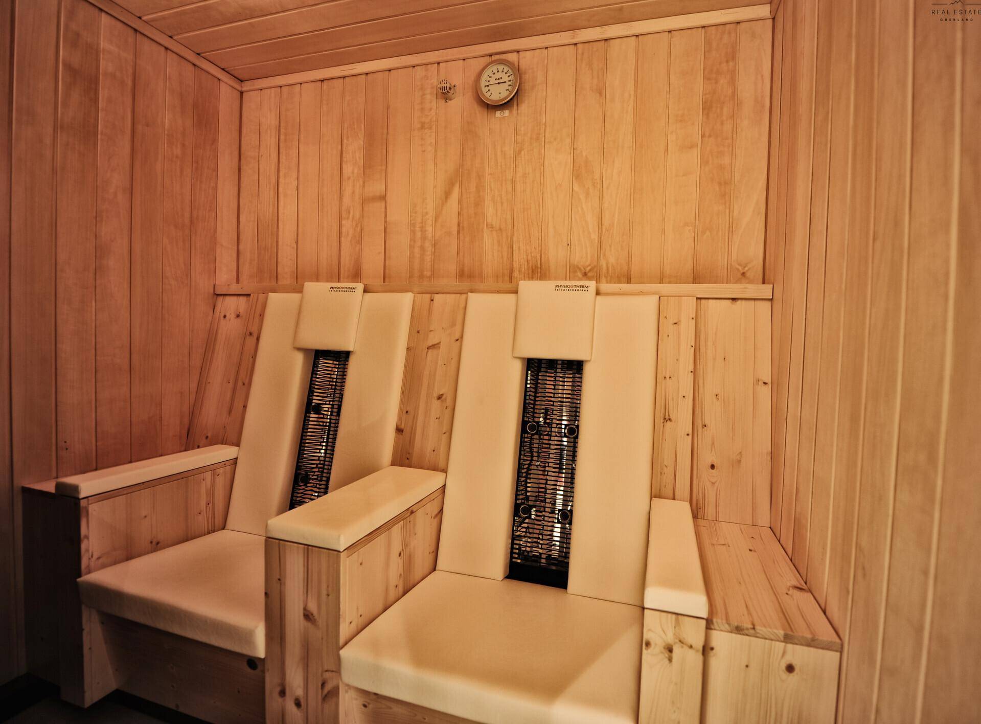 Innenansicht einer traditionellen Sauna mit Holzbänken und einem Thermometer an der Wand.
