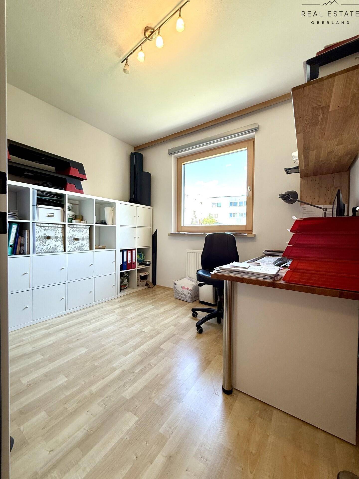 Helles Arbeitszimmer mit Laminatboden, großem Fenster und praktischen Regalsystemen.