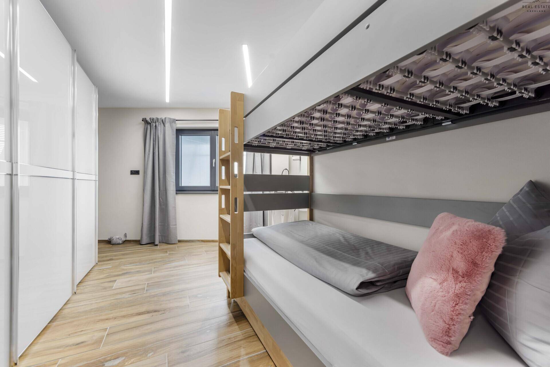 Kinder- oder Gästezimmer mit Etagenbett, weißen Einbauschränken und hellem Fenster.