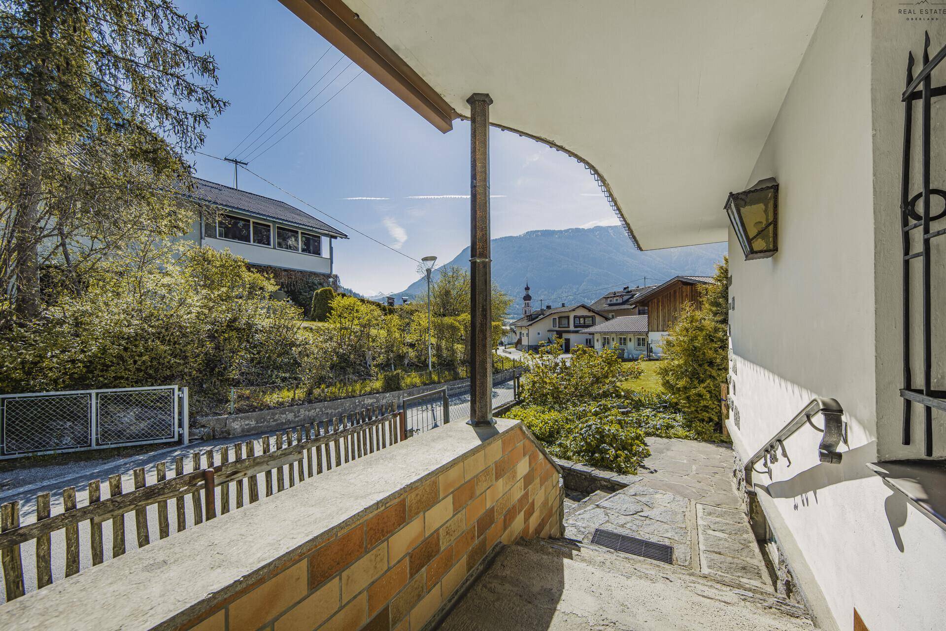 Eingangsbereich mit Treppe und Geländer, bietet einen Blick auf die Straße und die Berglandschaft.