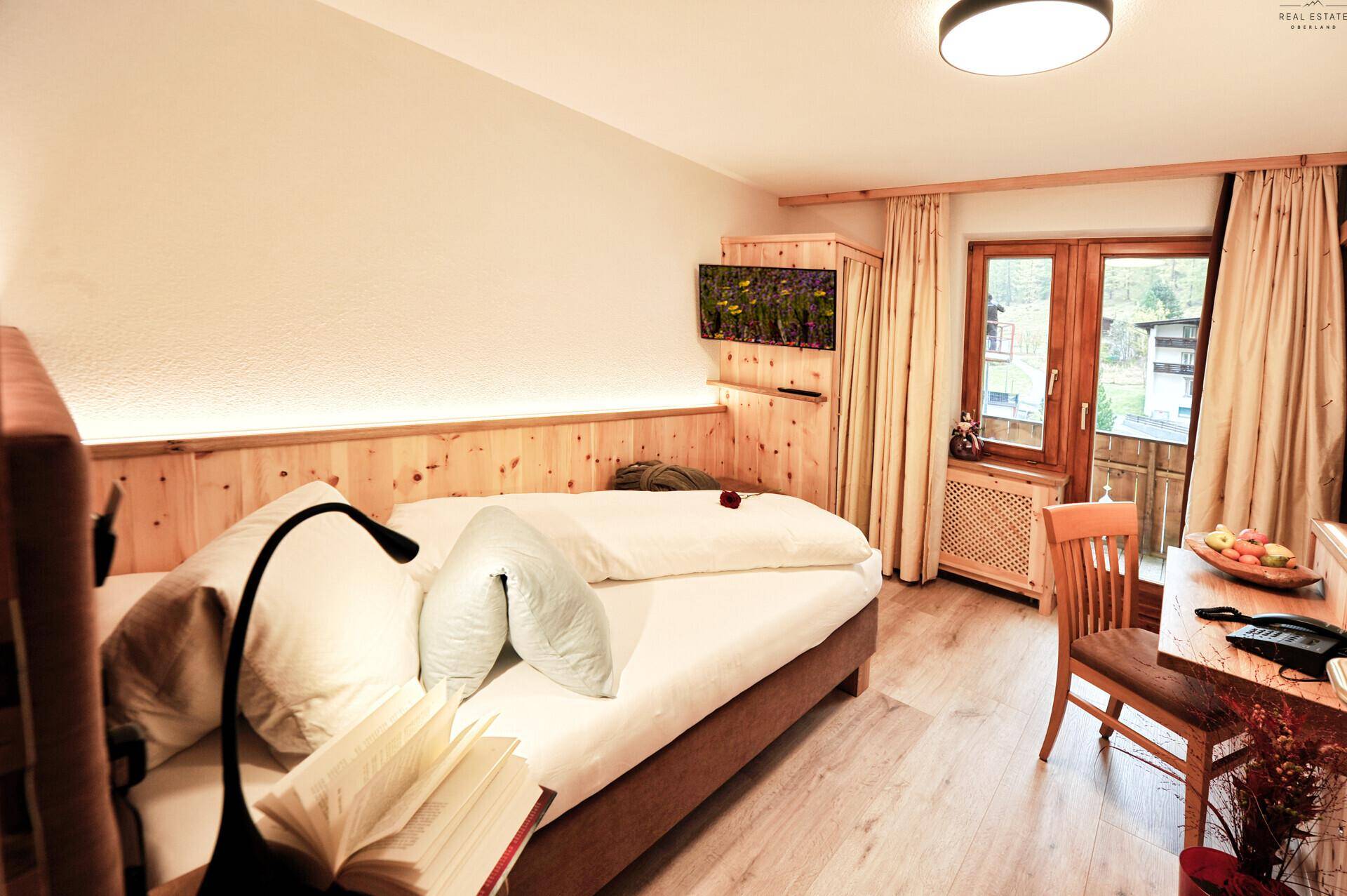 Einzelzimmer mit Holzwandverkleidung, kleinem Fernseher und Zugang zu einem Balkon.