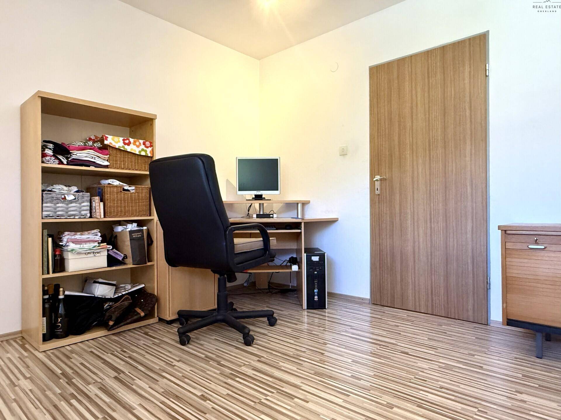 Funktionales Arbeitszimmer mit Schreibtisch, Bürostuhl und Holzregal.