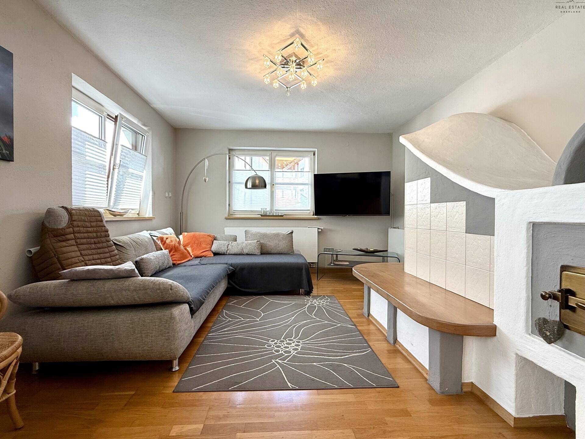 Geräumiges Wohnzimmer mit Kachelofen, Holzboden und großem Sofa.