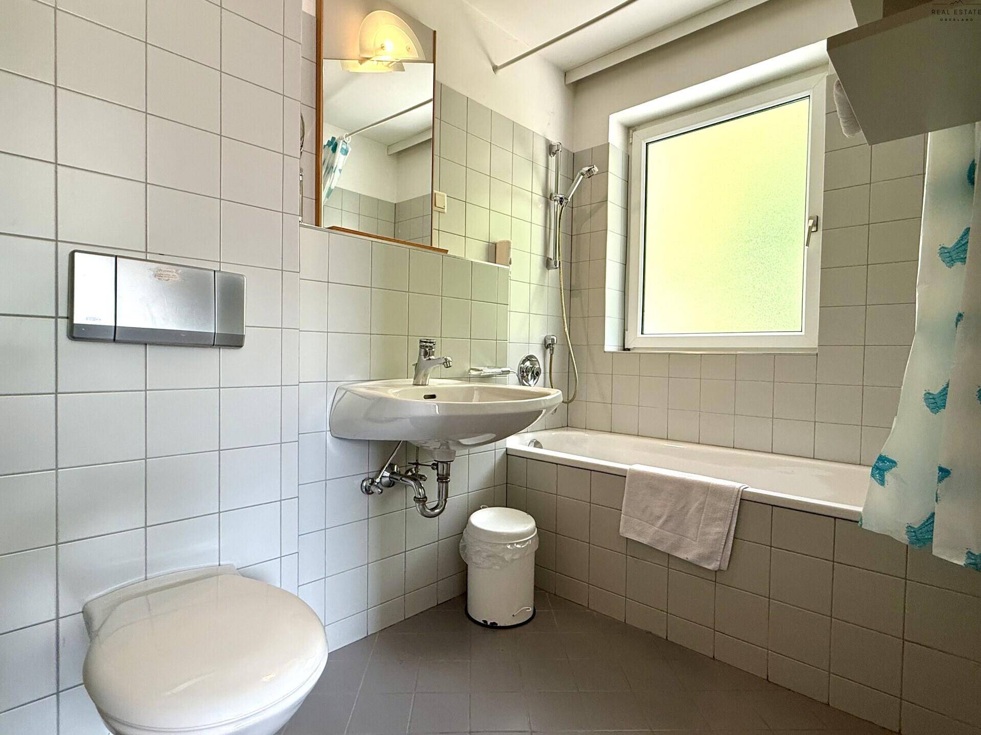 Helles Badezimmer mit Badewanne, WC, Waschbecken und einem Fenster für Tageslicht.