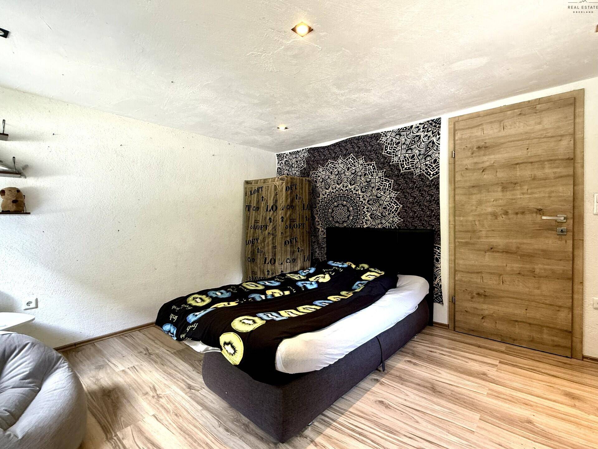 Gemütliches Schlafzimmer mit Einzelbett, Holzboden und dekorativer Wandgestaltung.