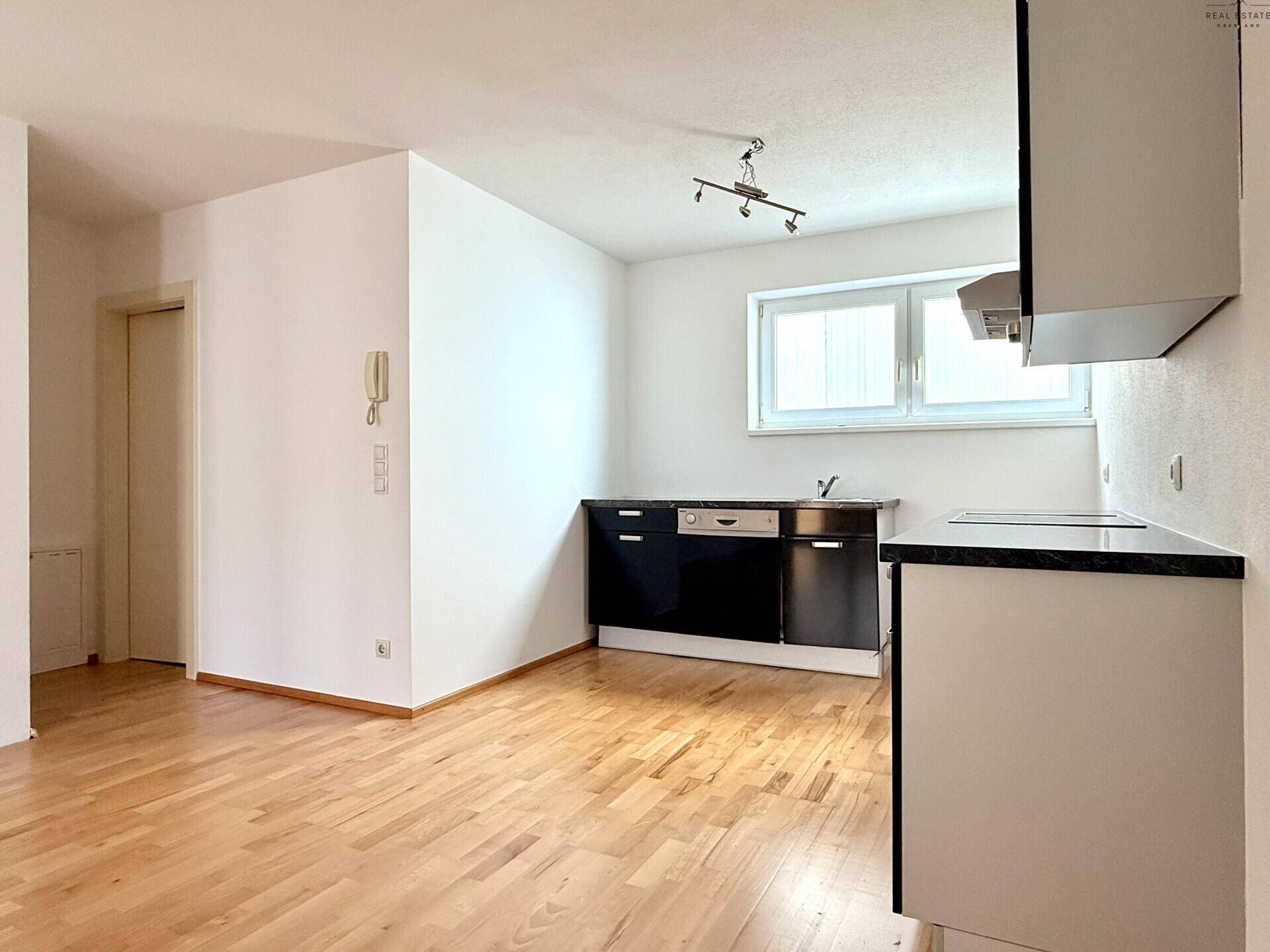Küchenbereich mit schwarzer Einbauküche, Holzboden und Fenster für natürliches Licht.