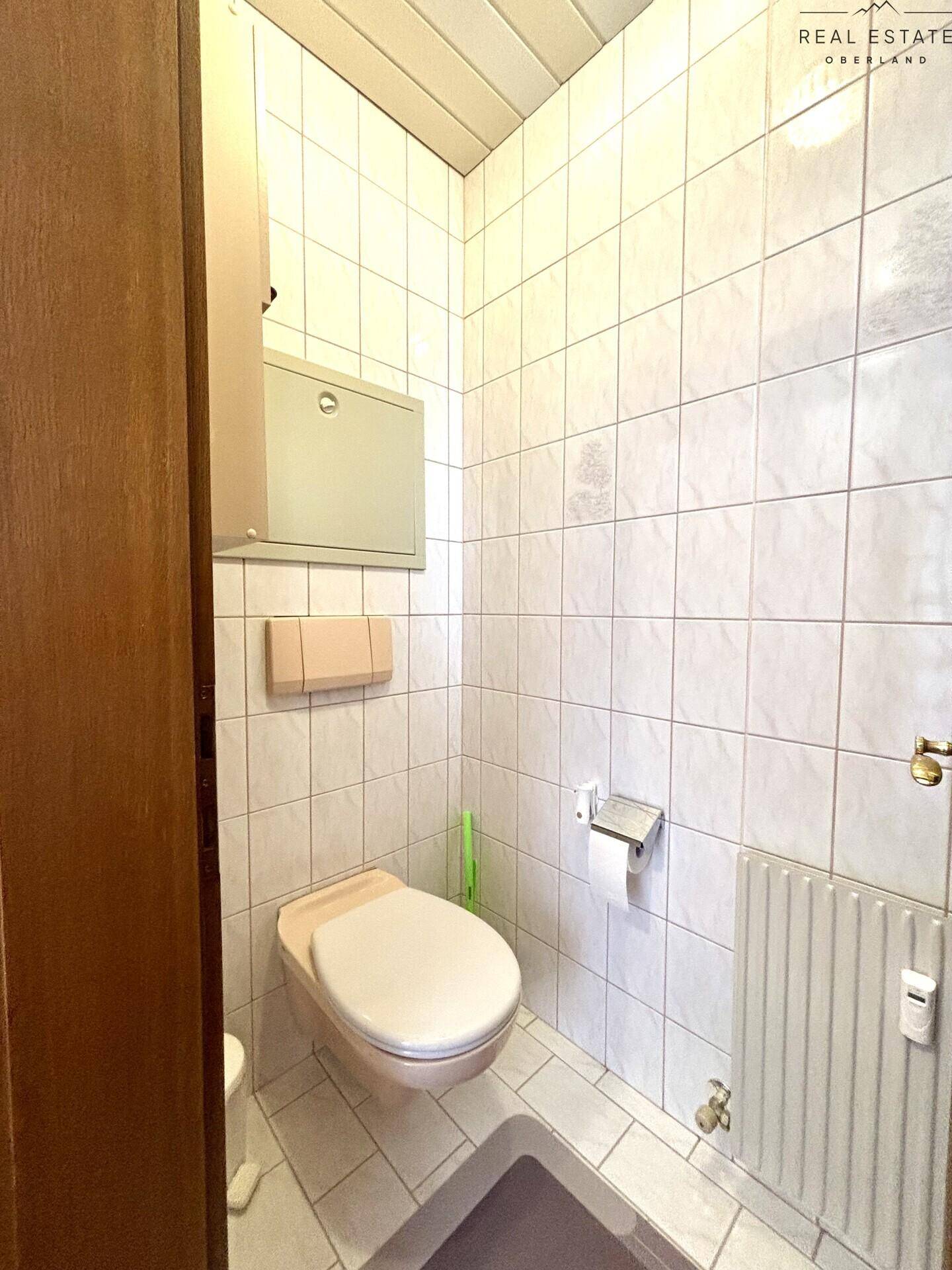 Separates WC mit Wandtoilette und hellen Fliesen, ausgestattet mit einem kleinen Heizkörper.