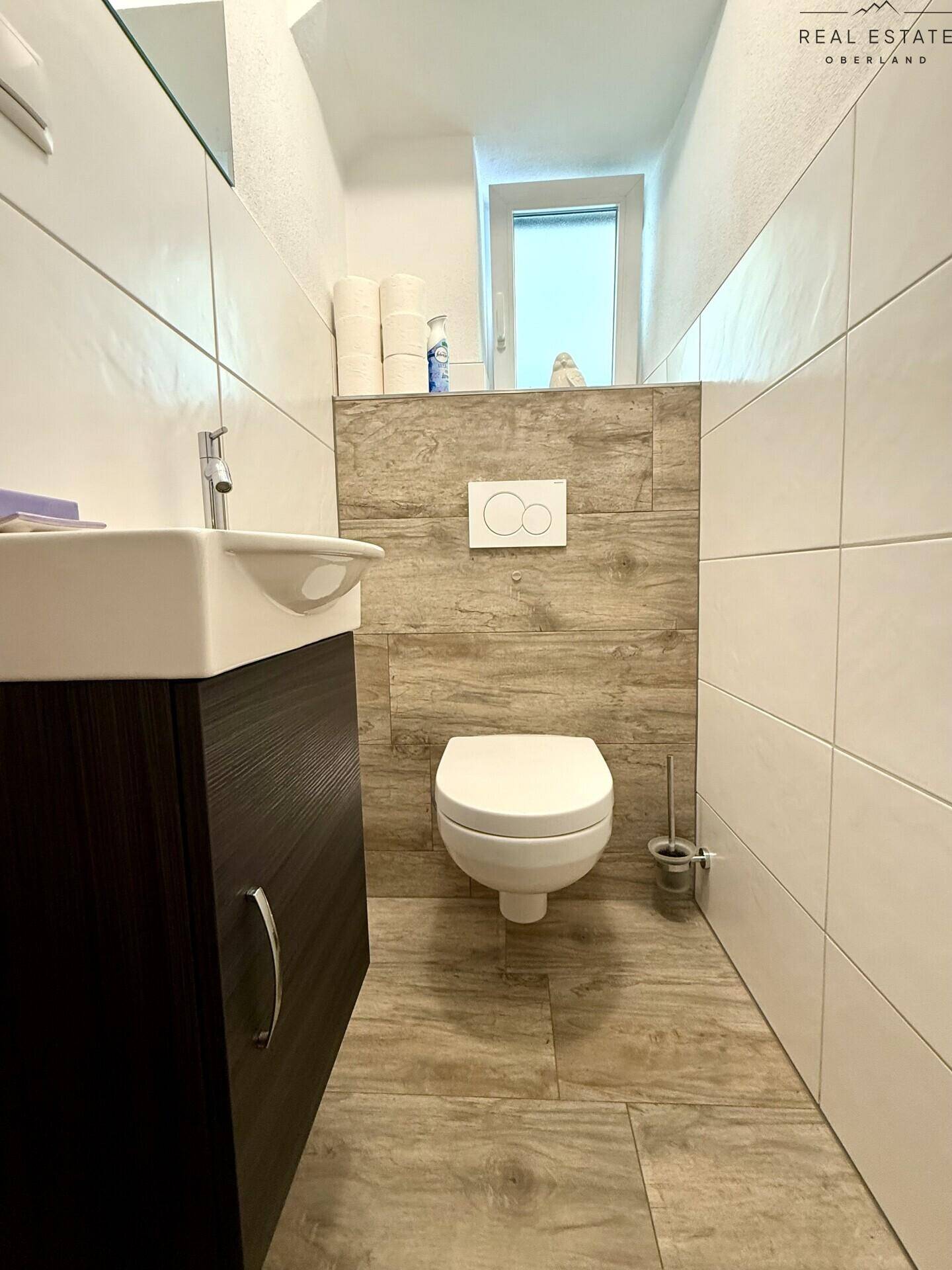 Modernes Gäste-WC mit Wand-WC, kleinem Waschbecken und Fliesen in Holzoptik.