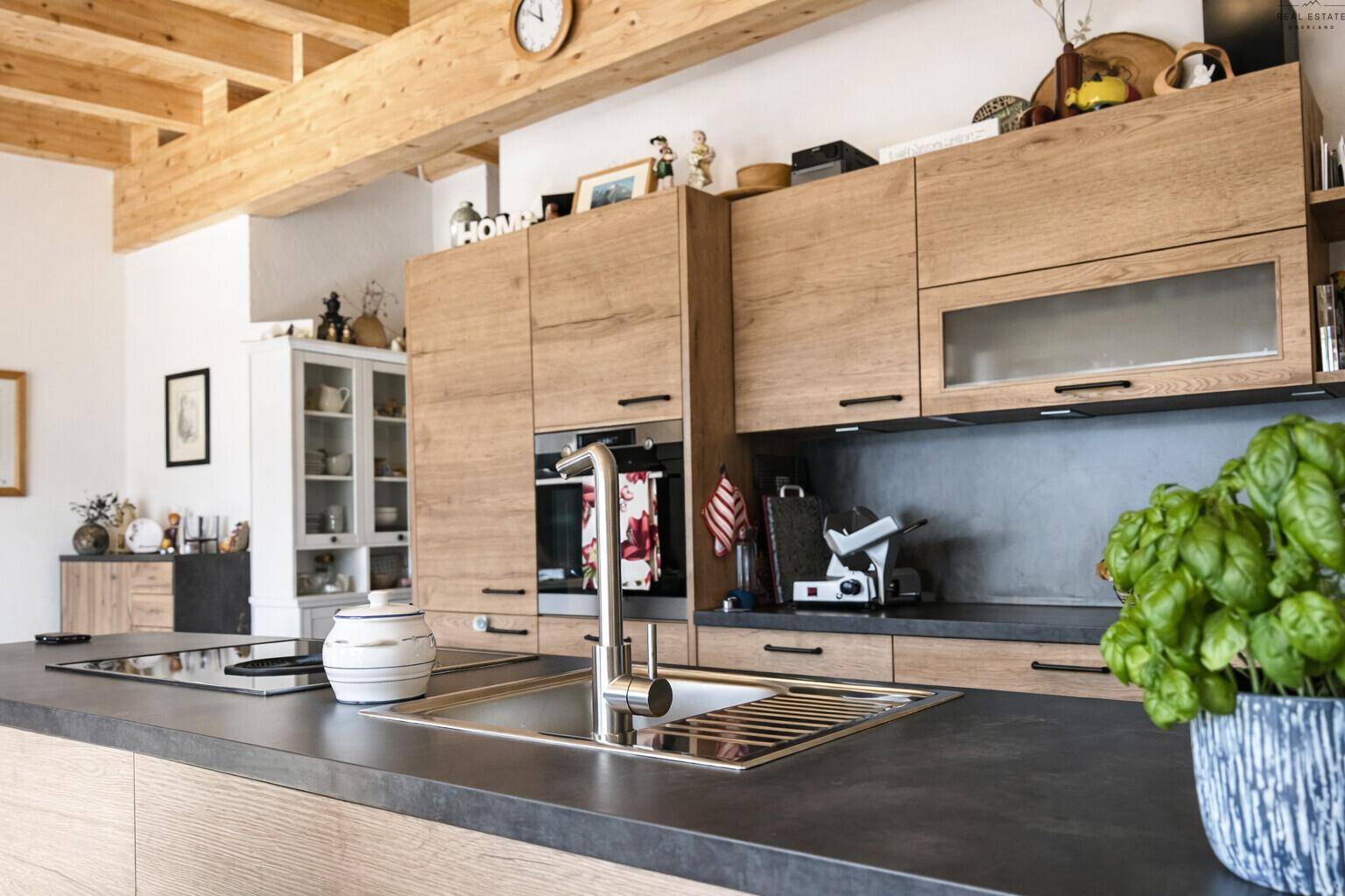 Moderne Holzküche mit dunkler Arbeitsplatte, integrierten Geräten und sichtbaren Deckenbalken.