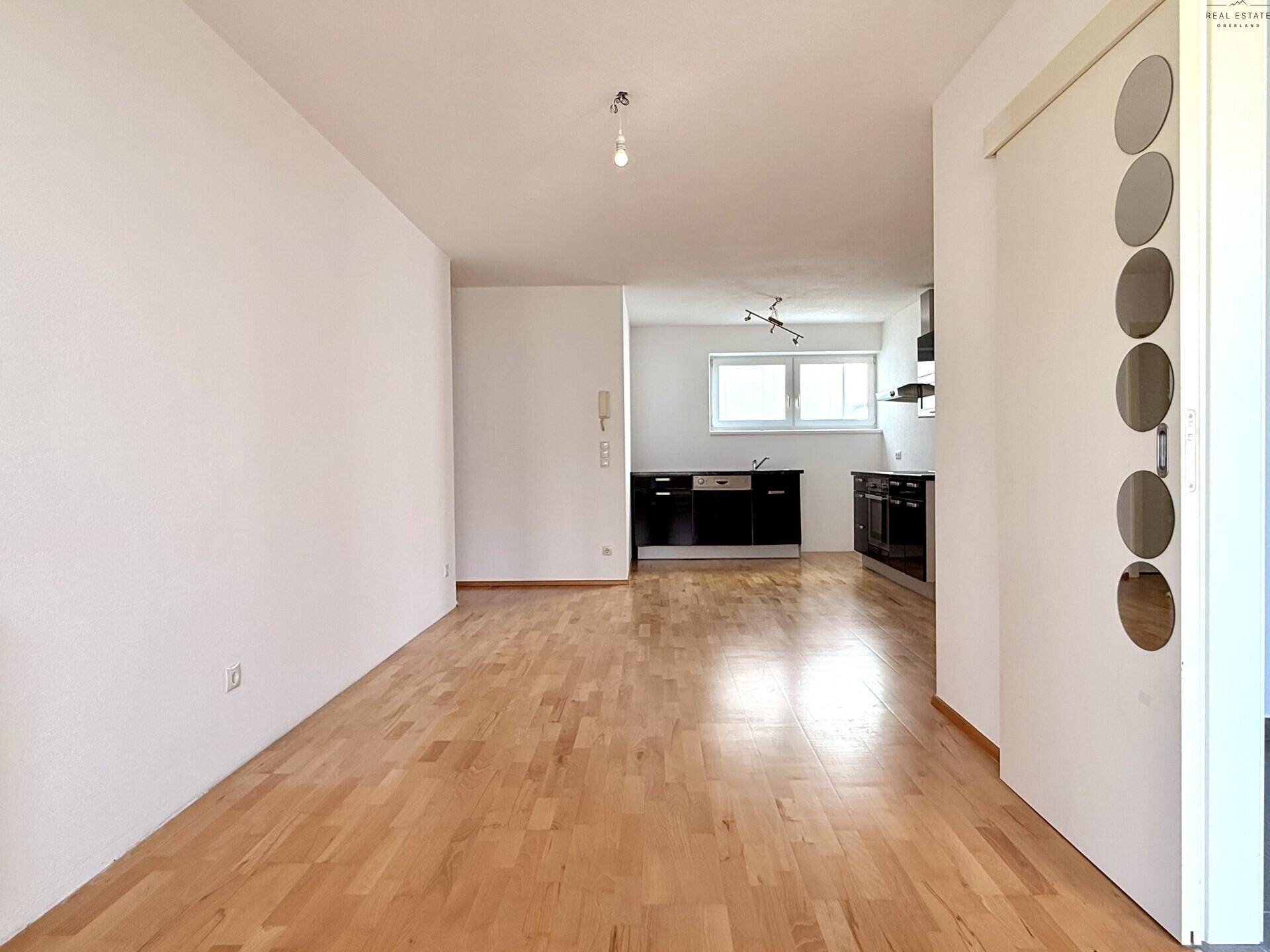 Offener Wohnbereich mit Holzboden und Blick auf die integrierte Küchenzeile.