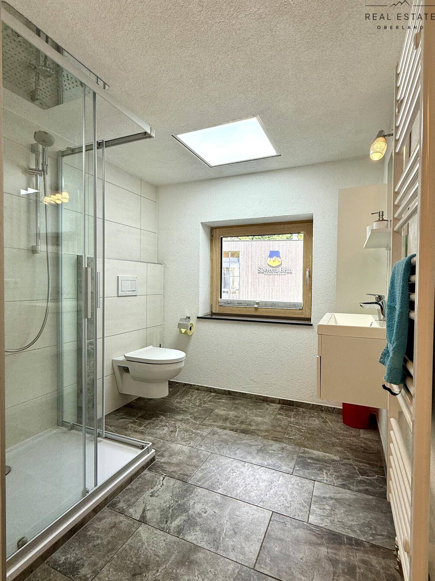 Modernes Badezimmer mit Dusche, WC, Waschbecken und Fenster für Tageslicht.