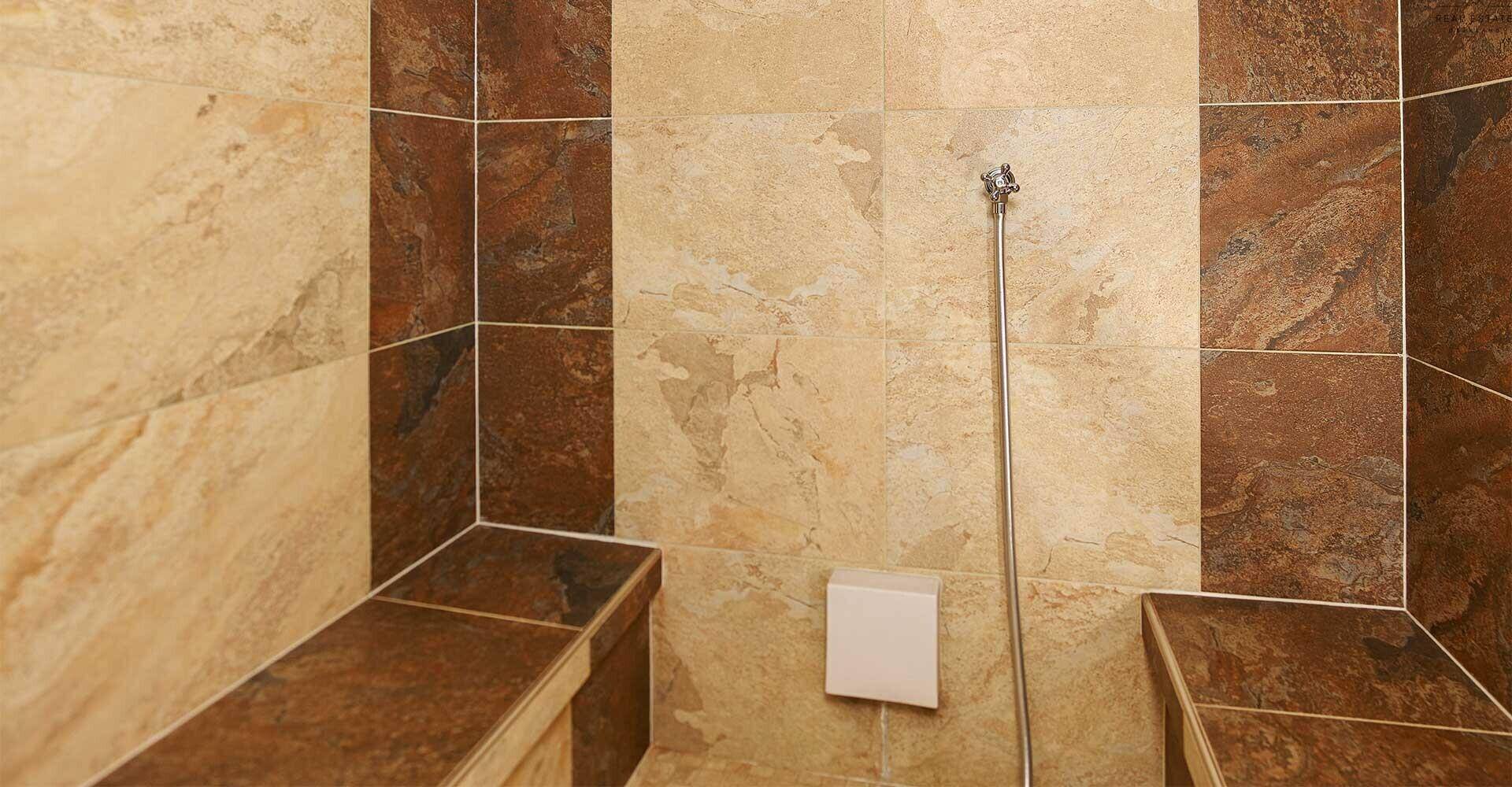 Dampfbad oder Duschbereich mit beigen und braunen Fliesen sowie integrierten Sitzbänken.