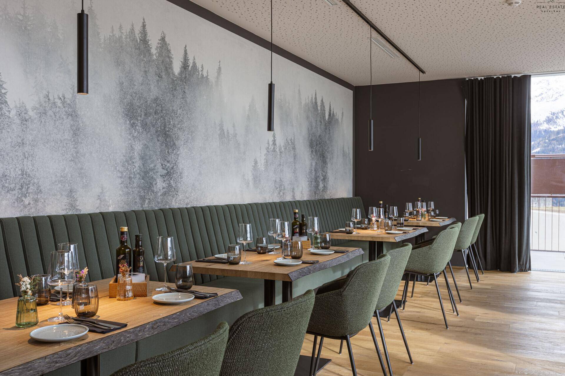 Gemütlicher Essbereich mit langer Sitzbank, Holztischen und einer stimmungsvollen Waldtapete an der Wand.