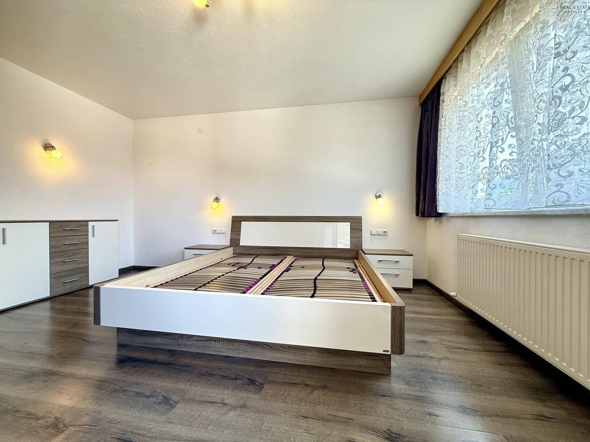 Schlafzimmer mit modernem Bett, Nachttischen und Laminatboden, hell und einladend gestaltet.
