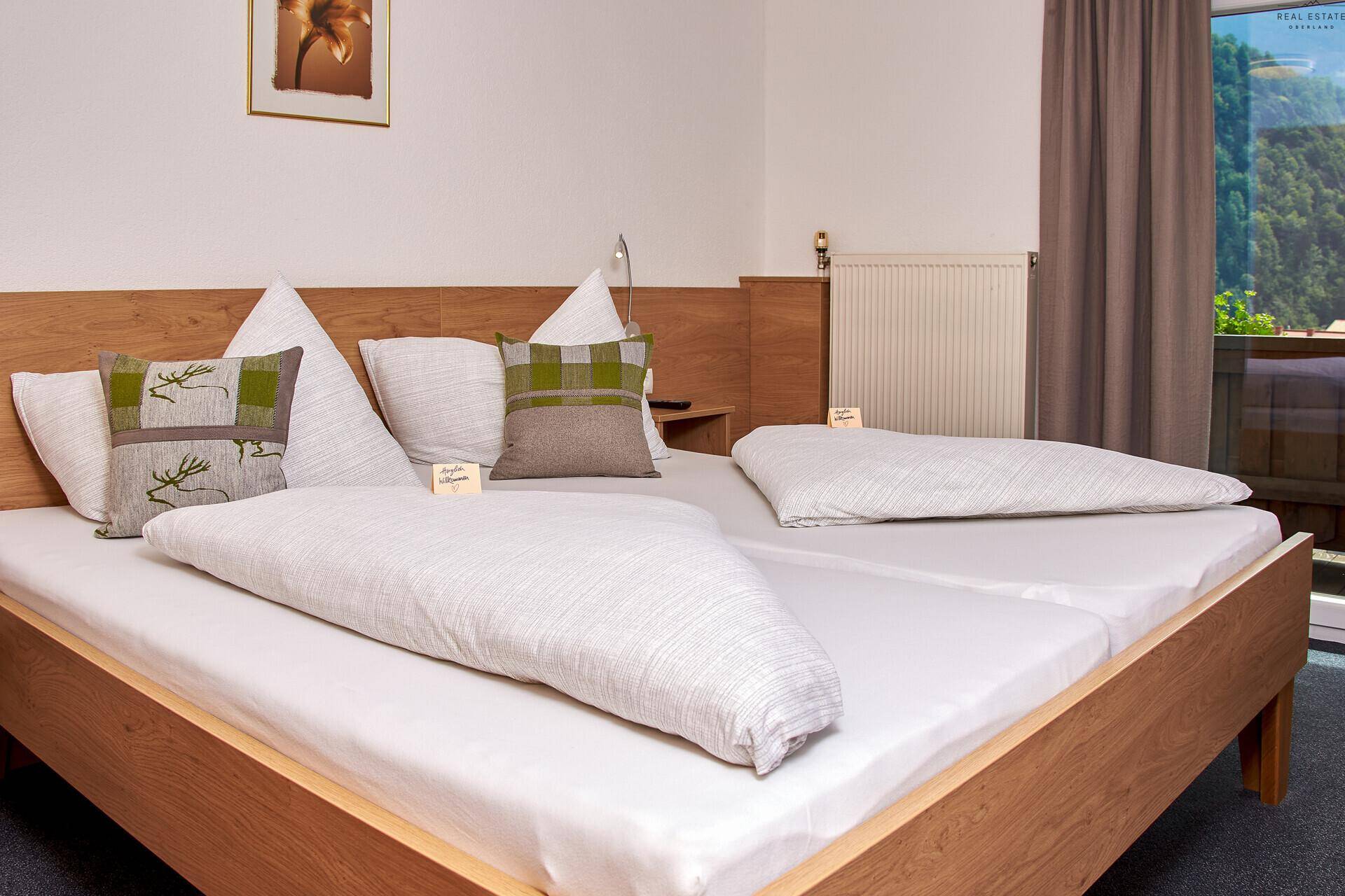 Schlafzimmer mit Doppelbett, Holzkopfteil und Blick auf die Berge durch die Balkontür.