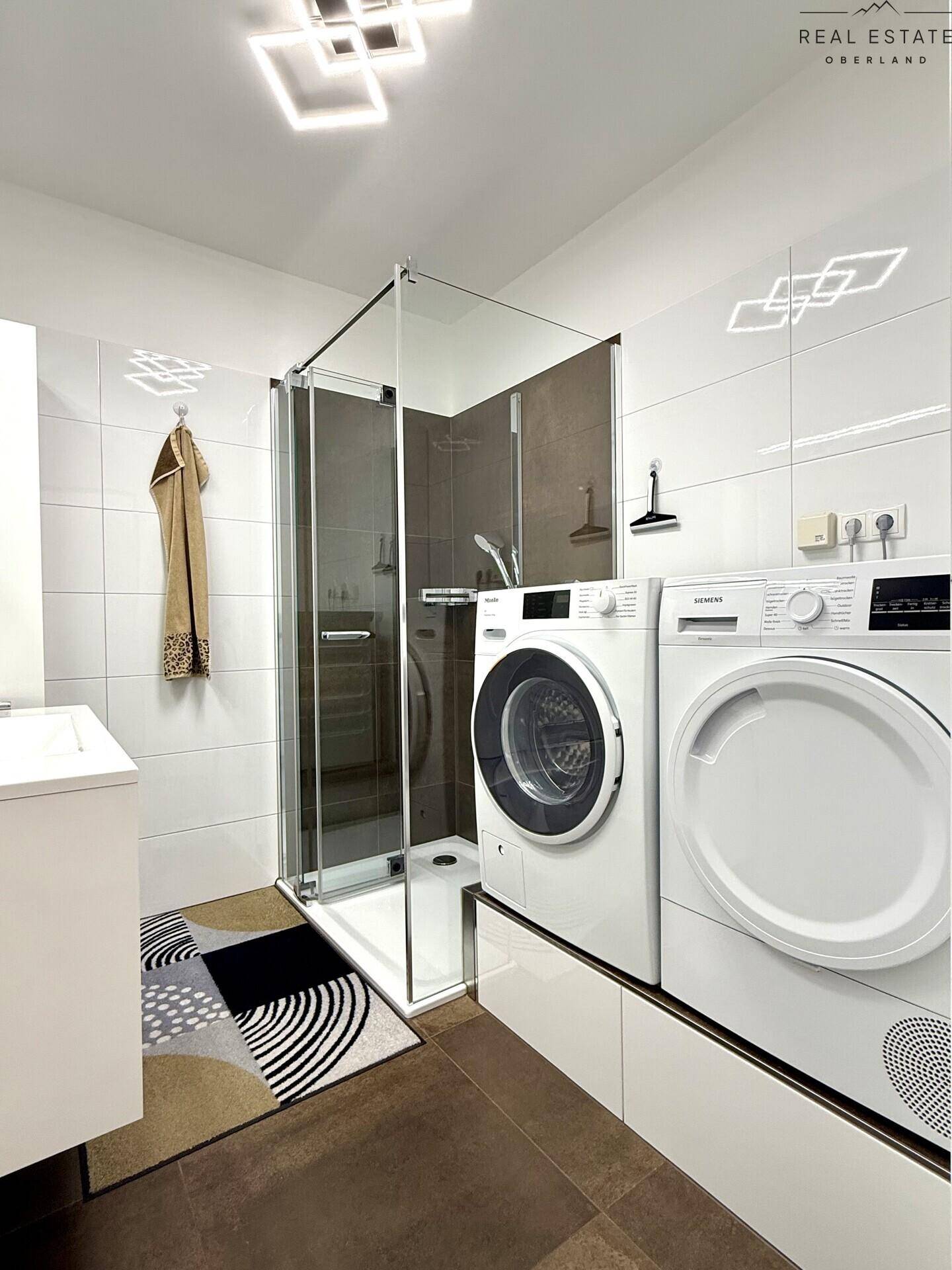 Modernes Badezimmer mit Dusche, Waschmaschine und Trockner, hell gefliest.