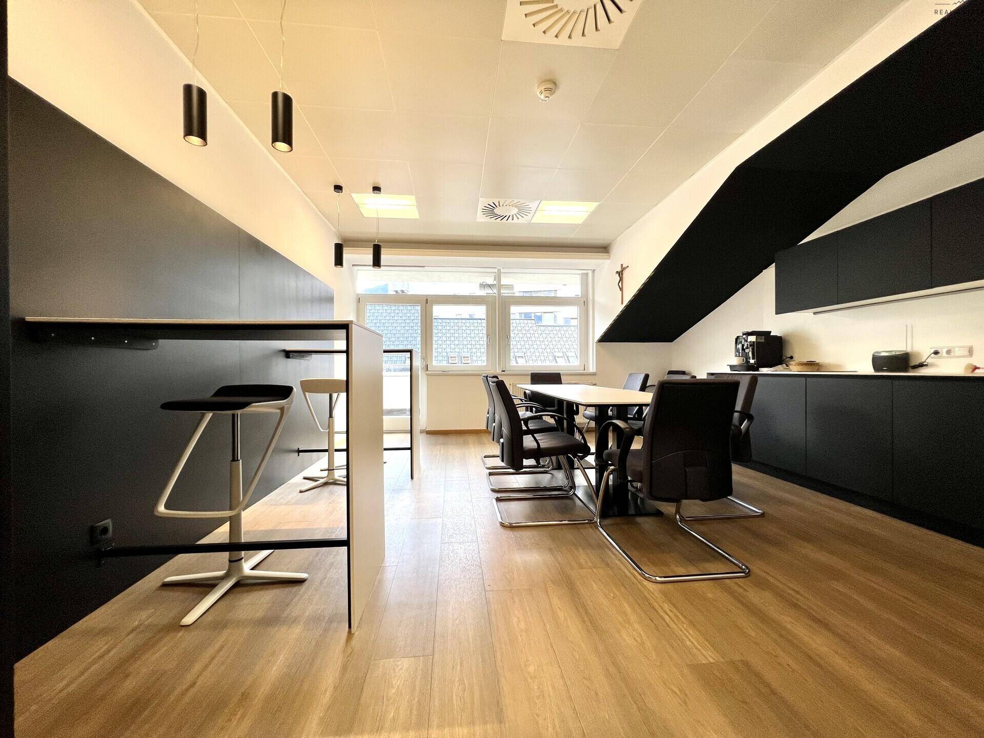 Moderne Büroküche mit schwarzer Einrichtung, Holzboden und einem Bartresen mit Hockern.