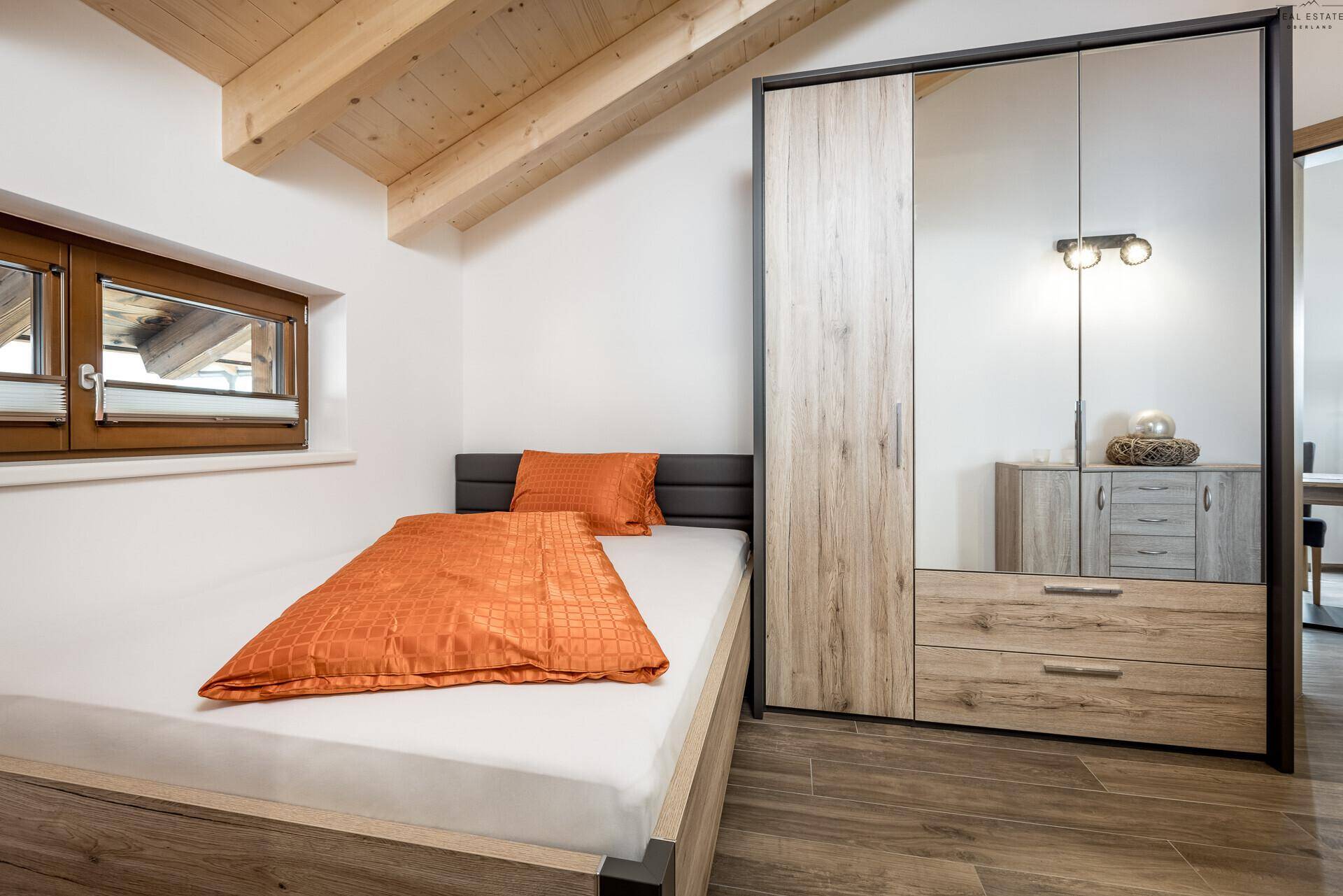 Gemütliches Schlafzimmer mit Einzelbett, Kleiderschrank und Holzbalkendecke.
