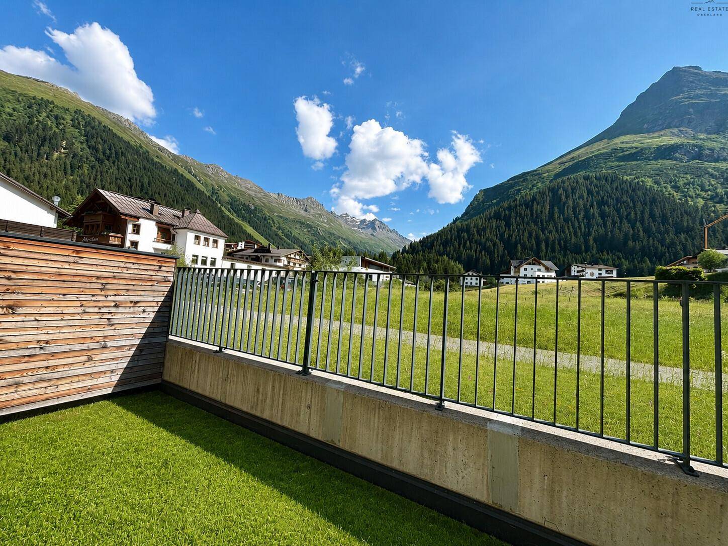 Grüne Rasenfläche mit Zaun und weitem Blick auf die umliegende Berglandschaft.
