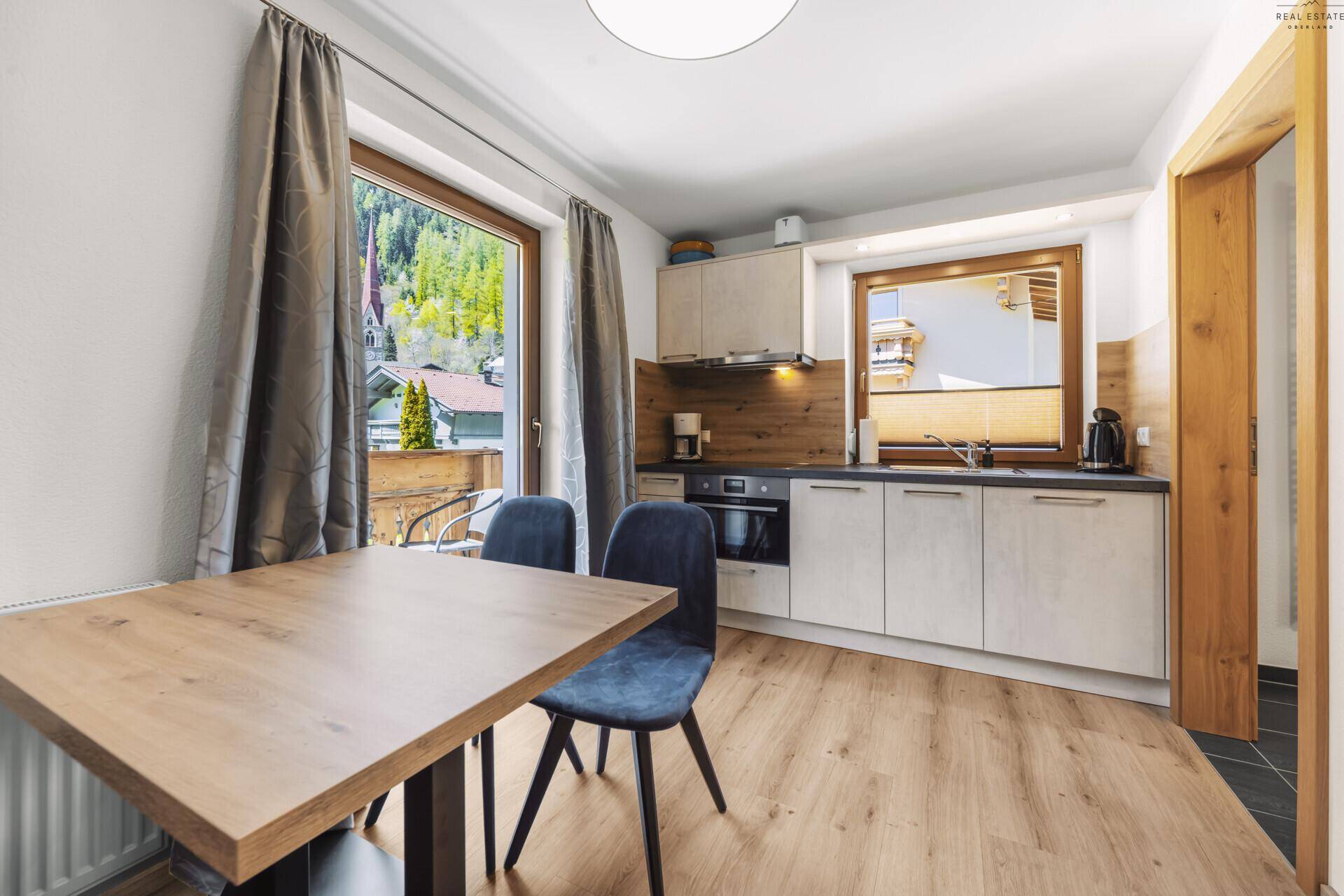 Moderne Wohnküche mit Essbereich, Holzboden und Zugang zu einem Balkon.