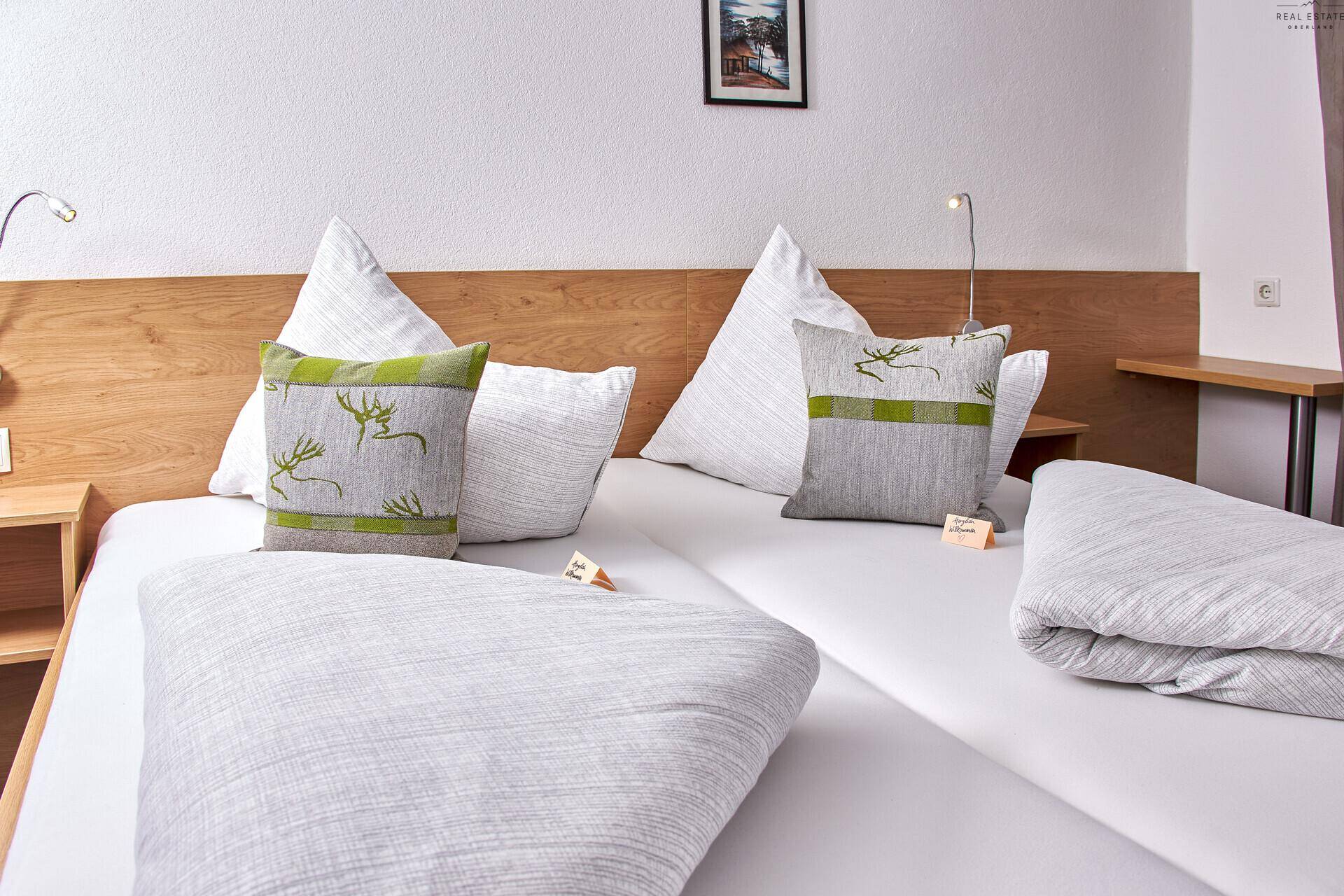 Gemütliches Schlafzimmer mit zwei Einzelbetten, Holzkopfteil und grünen Akzentkissen.