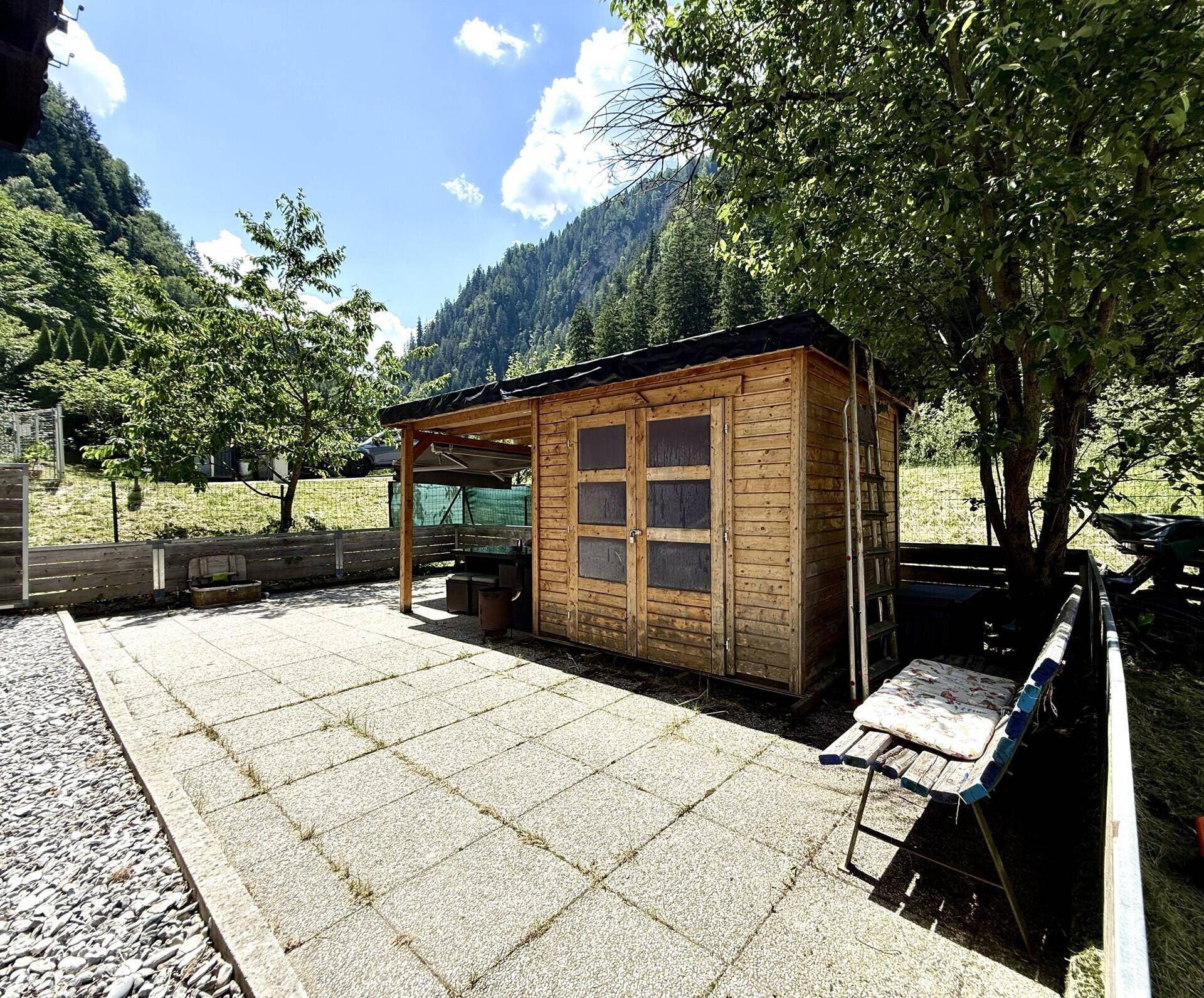 Gepflasterter Gartenbereich mit Holzschuppen und viel Grün, ideal für Freizeit im Freien.