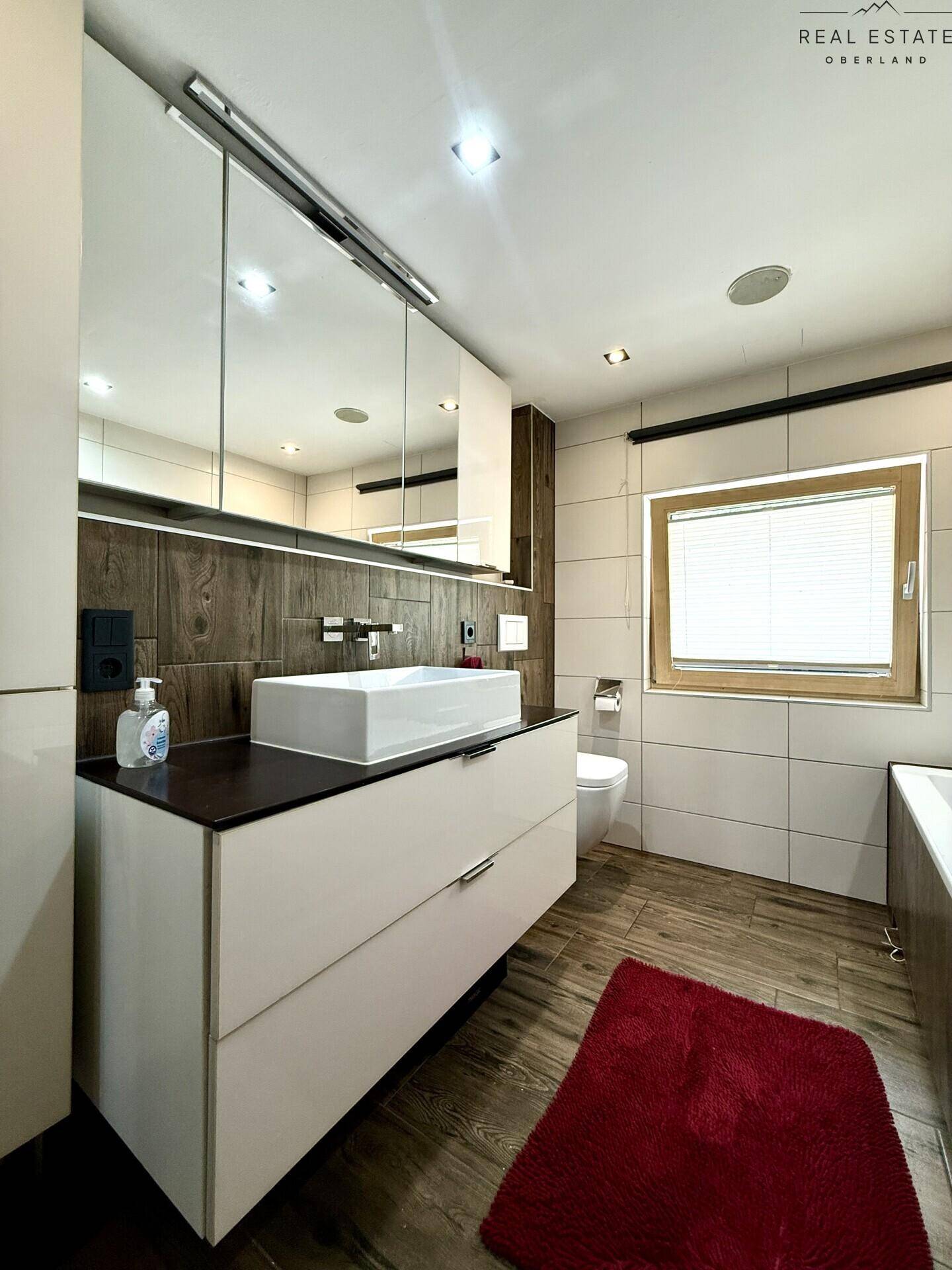 Stilvolles Badezimmer mit großem Waschbecken, Spiegelschrank und Fenster, in hellen Farben gehalten.