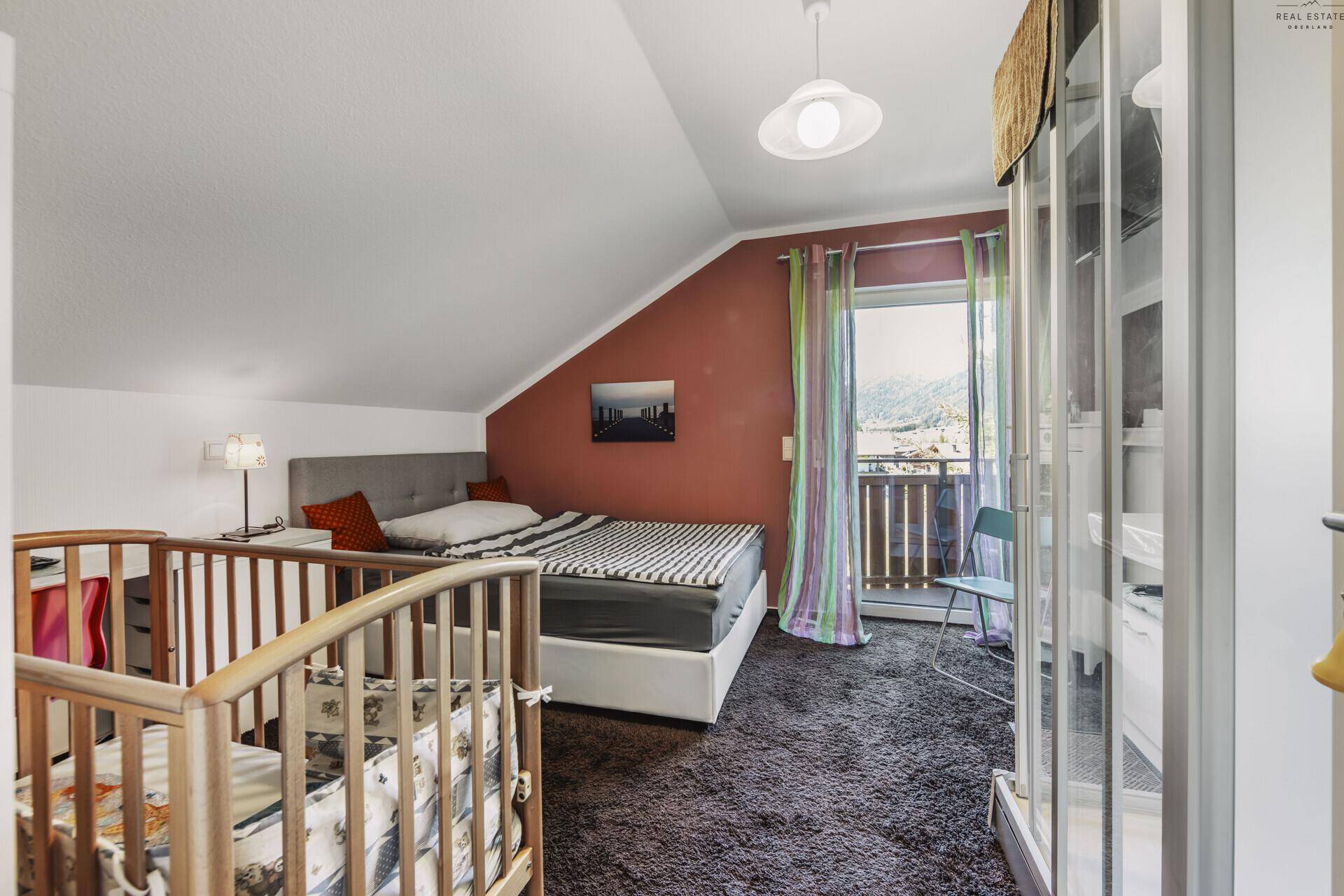 Gemütliches Schlafzimmer mit Kinderbett, Balkonzugang und Blick auf die Berge.