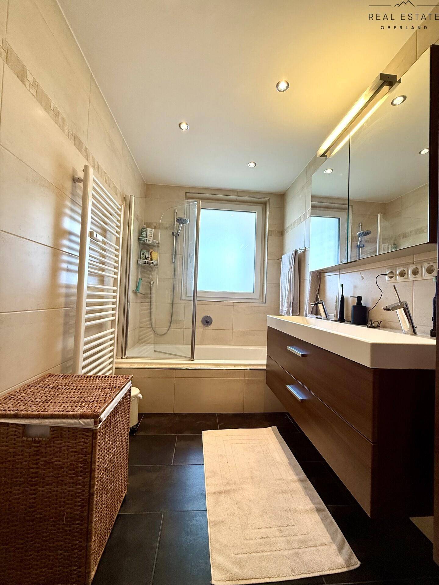 Helles Badezimmer mit Badewanne, Dusche, Waschbecken und Handtuchheizkörper.