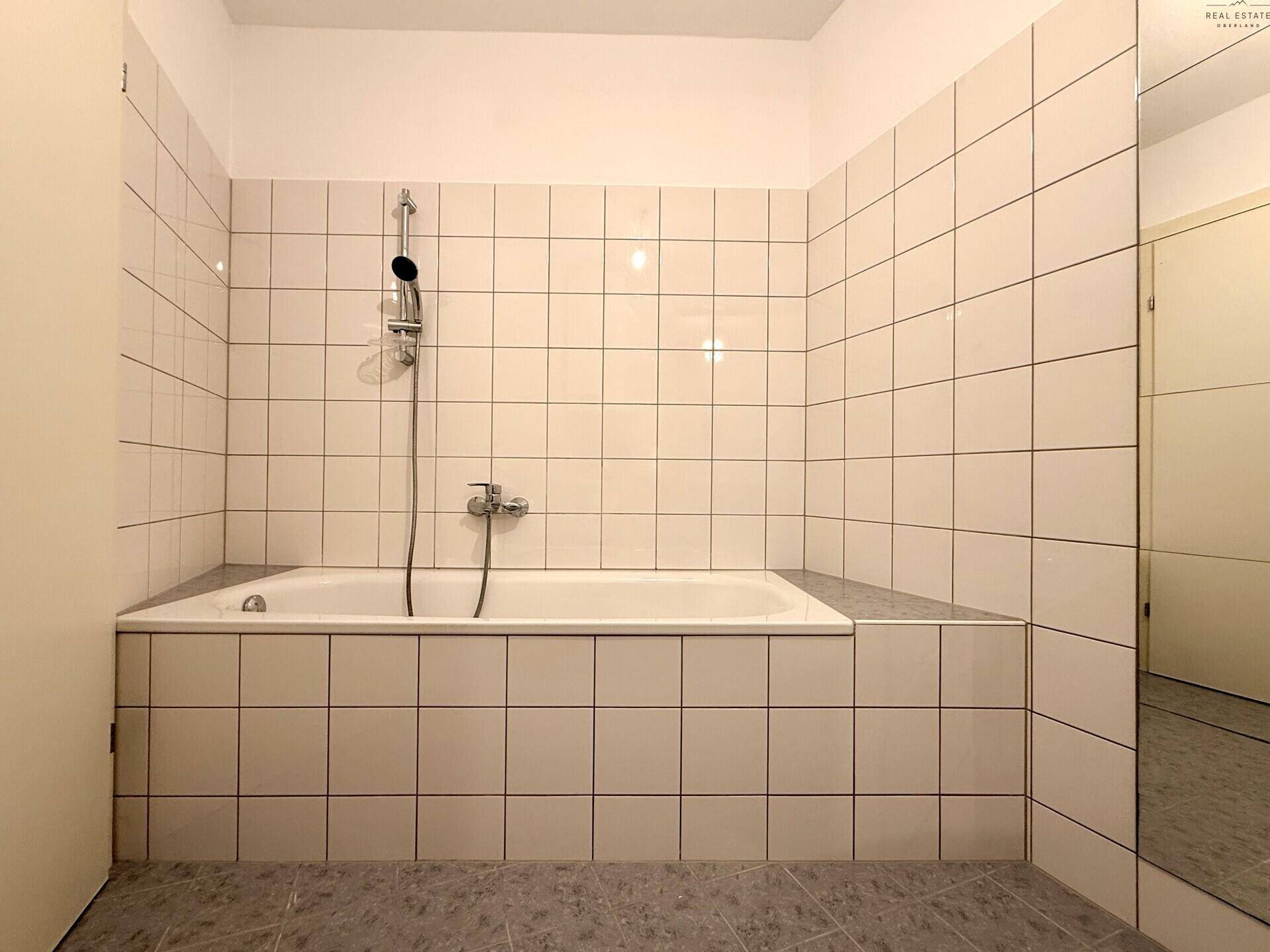 Badezimmer mit Badewanne, weißen Fliesen und Duscharmatur.