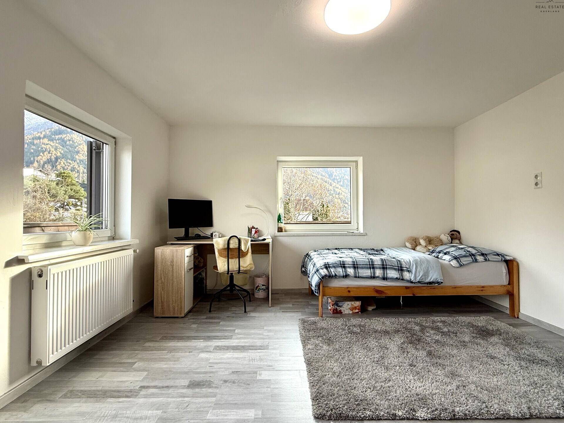 Helles Kinderzimmer mit Bett, Schreibtisch und Fenster mit Bergblick.