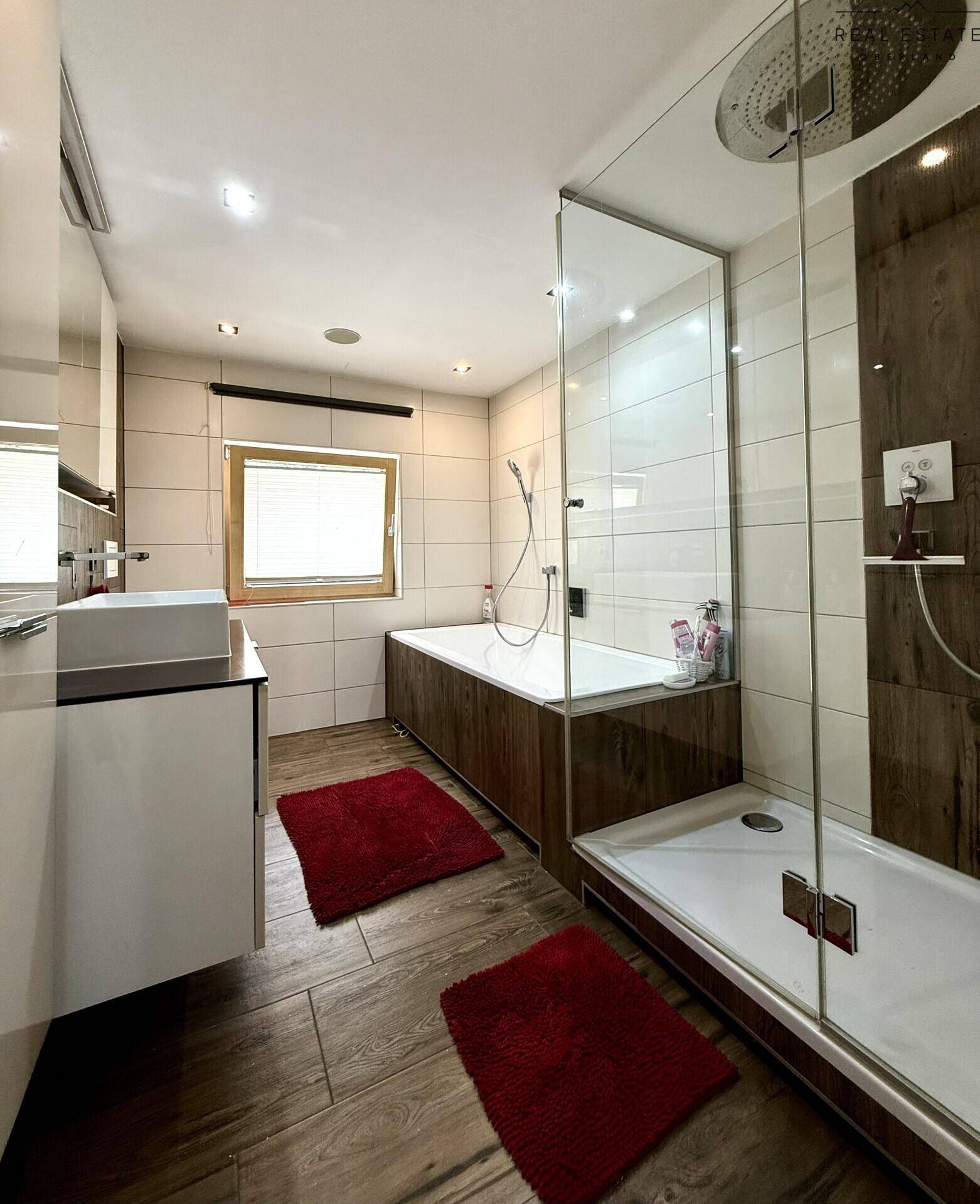 Modernes Badezimmer mit Badewanne, Glasdusche und Fenster, ausgestattet mit hochwertigen Fliesen.