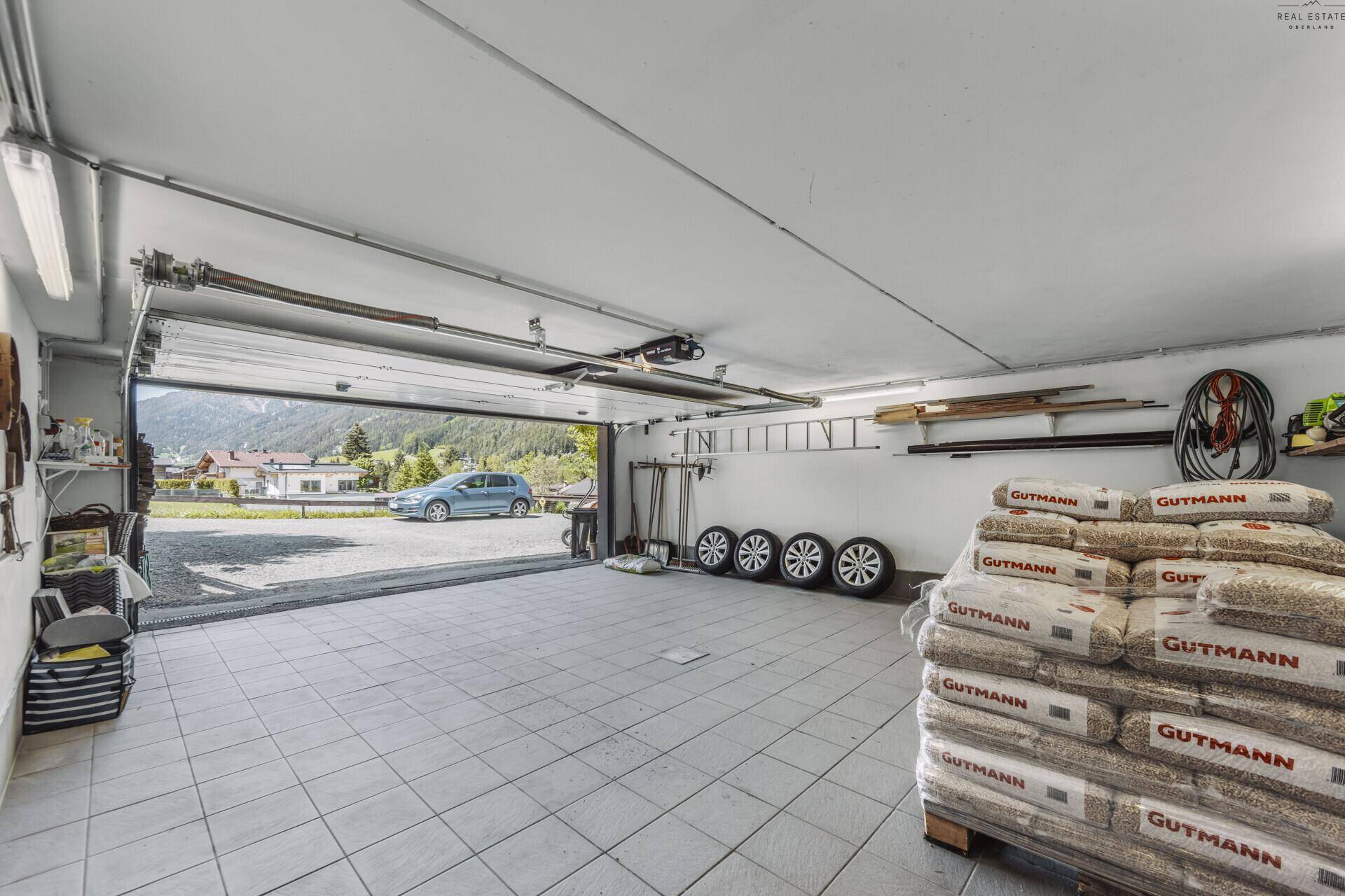 Geräumige Garage mit offenem Tor, Blick nach draußen und Lagerung für Holzpellets.