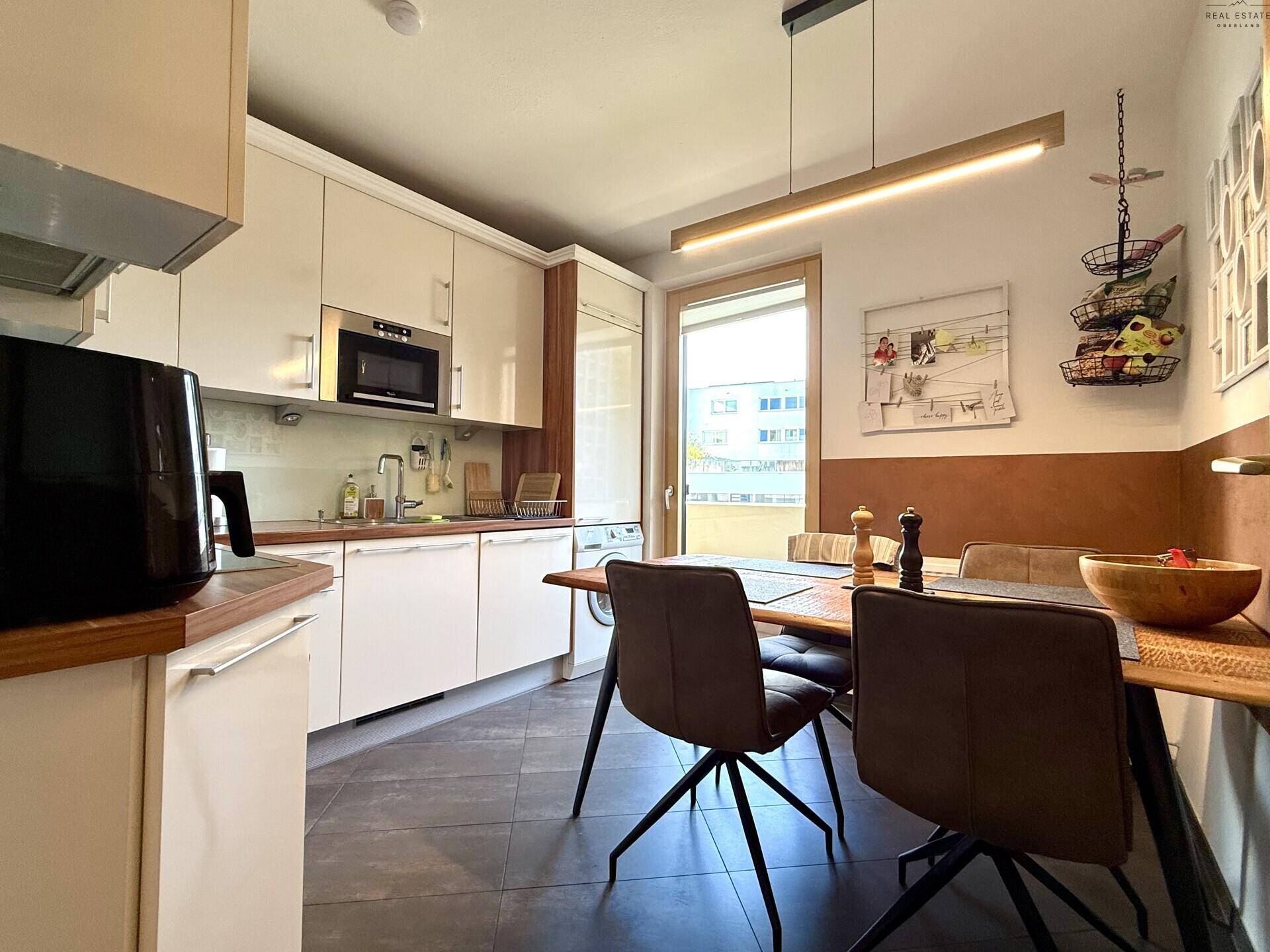 Helle Küche mit Essbereich, weißen Schränken und Zugang zum Balkon.