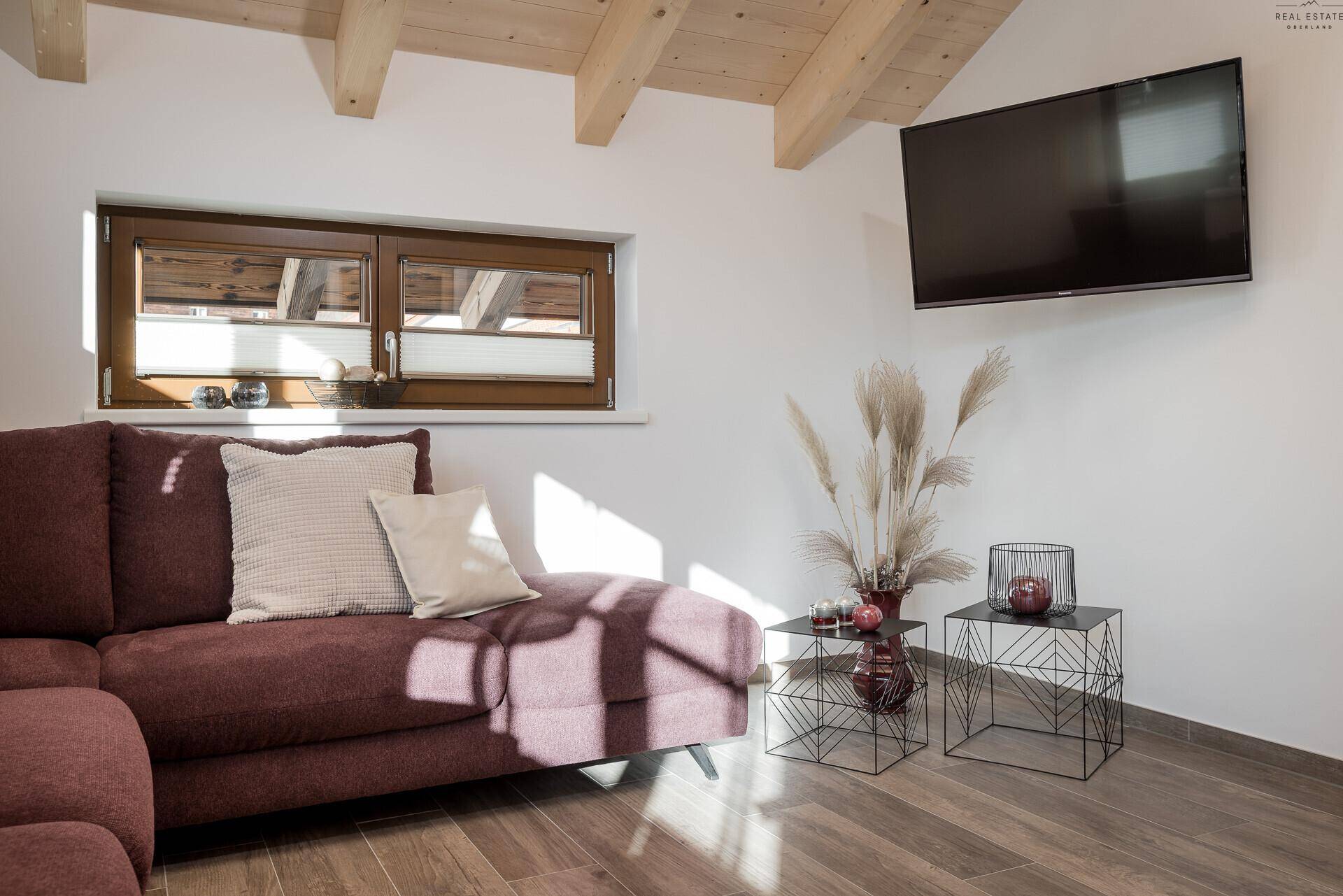 Gemütliches Wohnzimmer mit Holzbalkendecke, Sofa und Wandfernseher.