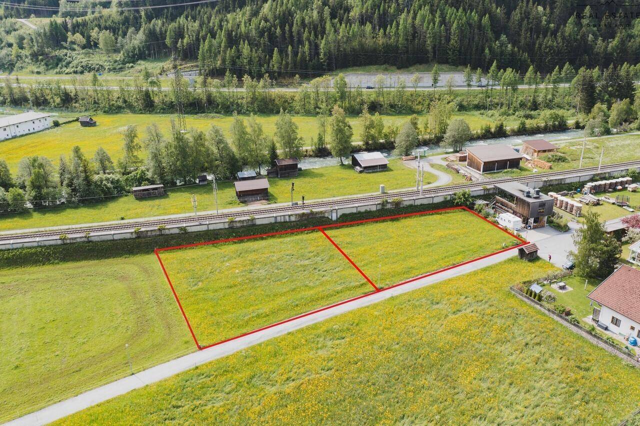 Luftaufnahme von zwei Grundstücken, begrenzt durch rote Linien, neben Bahngleisen und einem Fluss.
