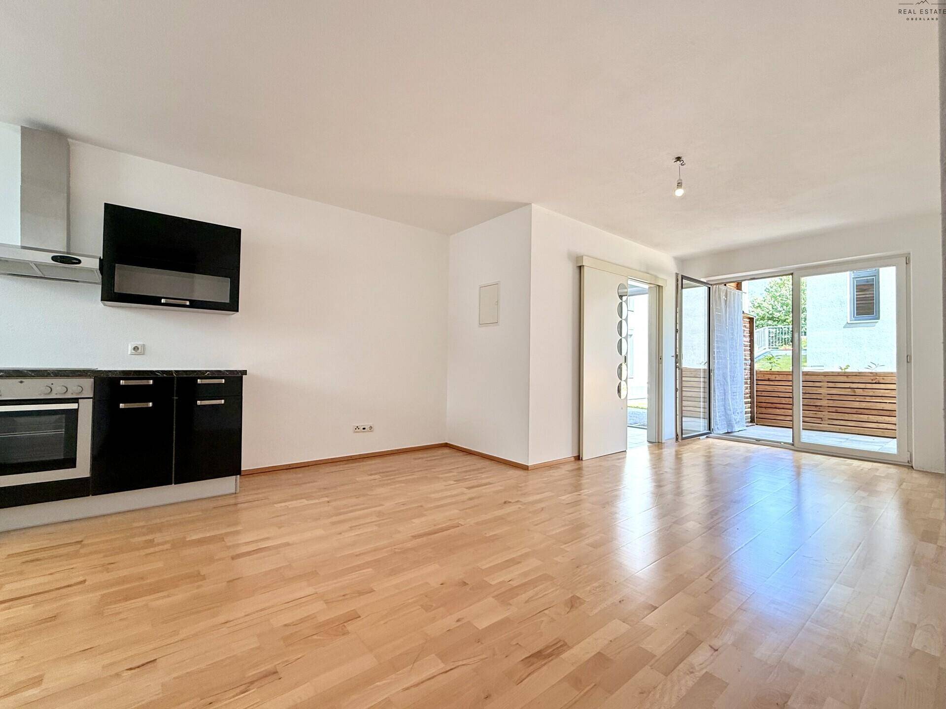 Geräumiger Wohnbereich mit Holzboden, Küchenzeile und großen Fenstern zur Terrasse.