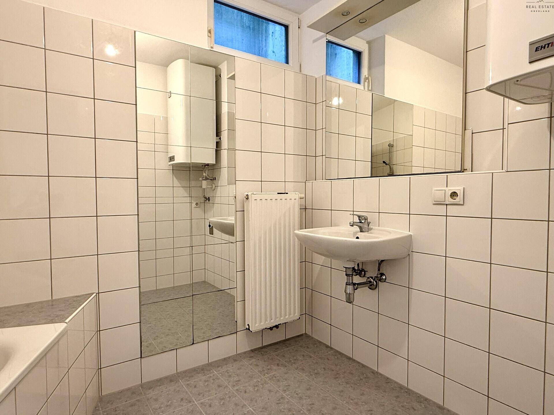 Helles Badezimmer mit Waschbecken, Spiegel und Fenster für natürliche Belüftung.