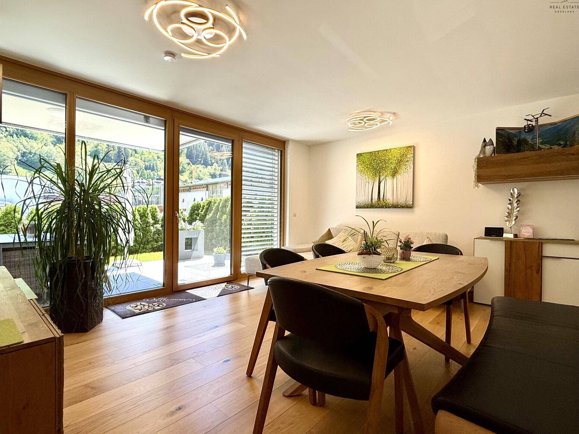 Lichtdurchfluteter Wohn-Essbereich mit Esstisch, Sofa und großen Fenstern zur Terrasse.