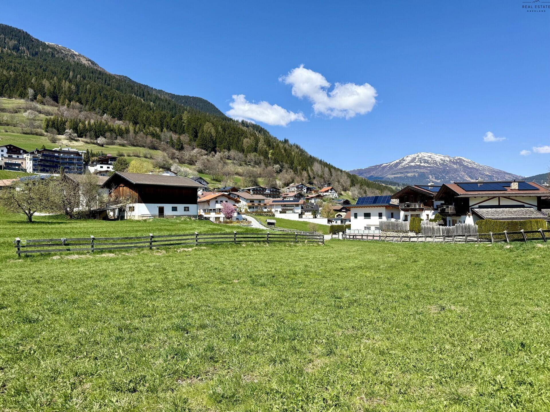 Idyllische Landschaft mit weiten grünen Feldern, einem charmanten Dorf und imposanten Bergen am Horizont.